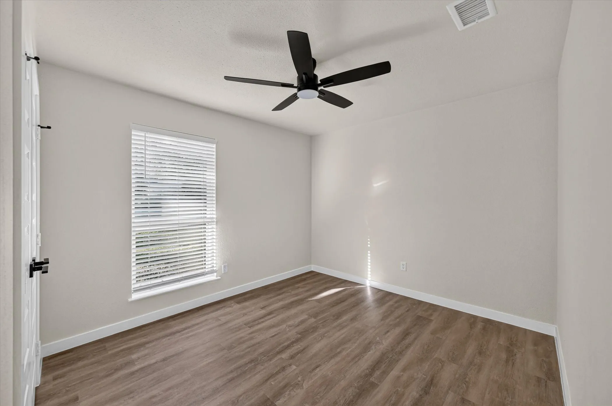 Neutral-toned walls, wood-finish flooring, single window with blinds, ceiling fan, and white trim