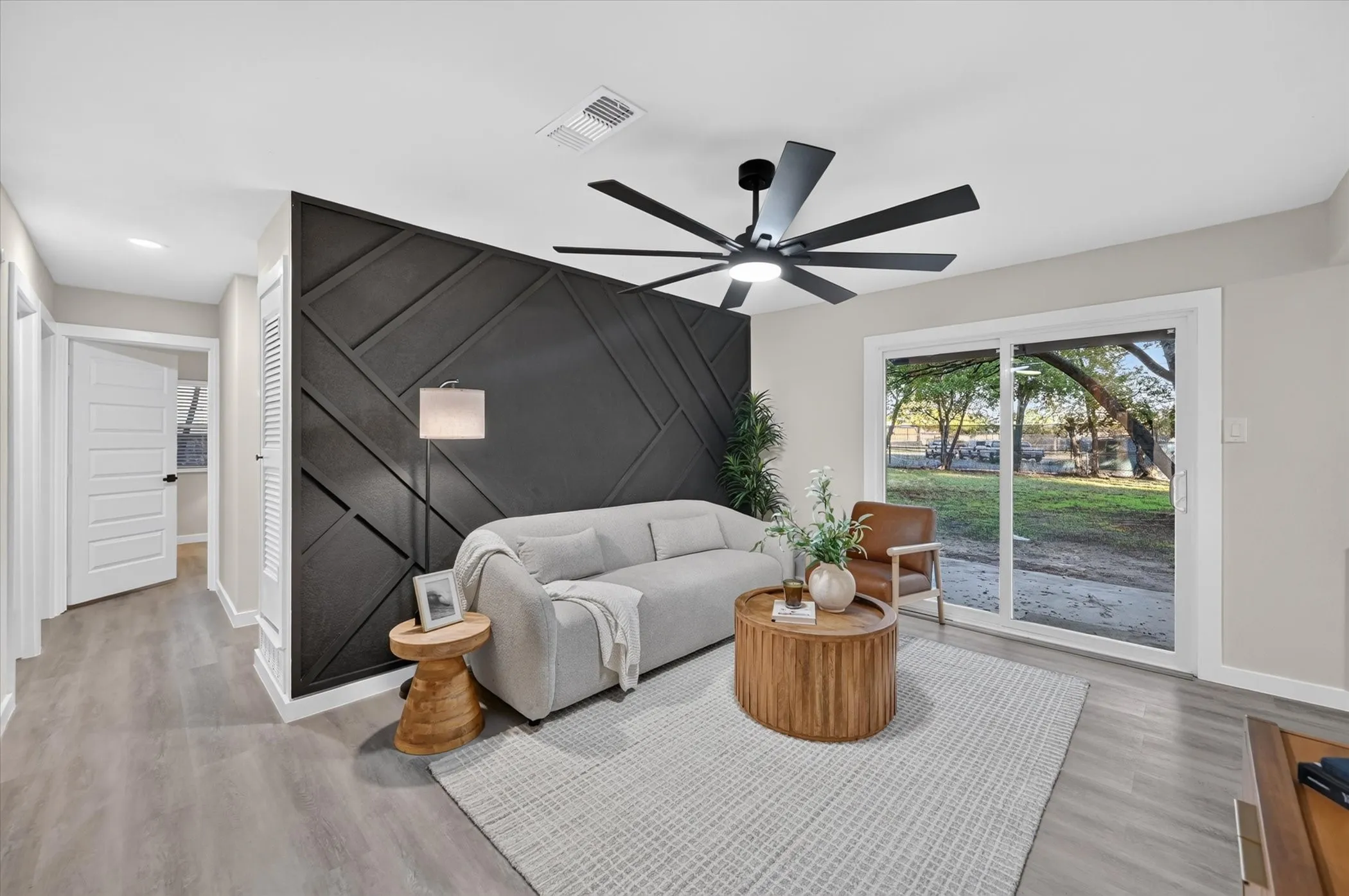 Wood-finish flooring, accent wall with geometric paneling, and a contemporary ceiling fan