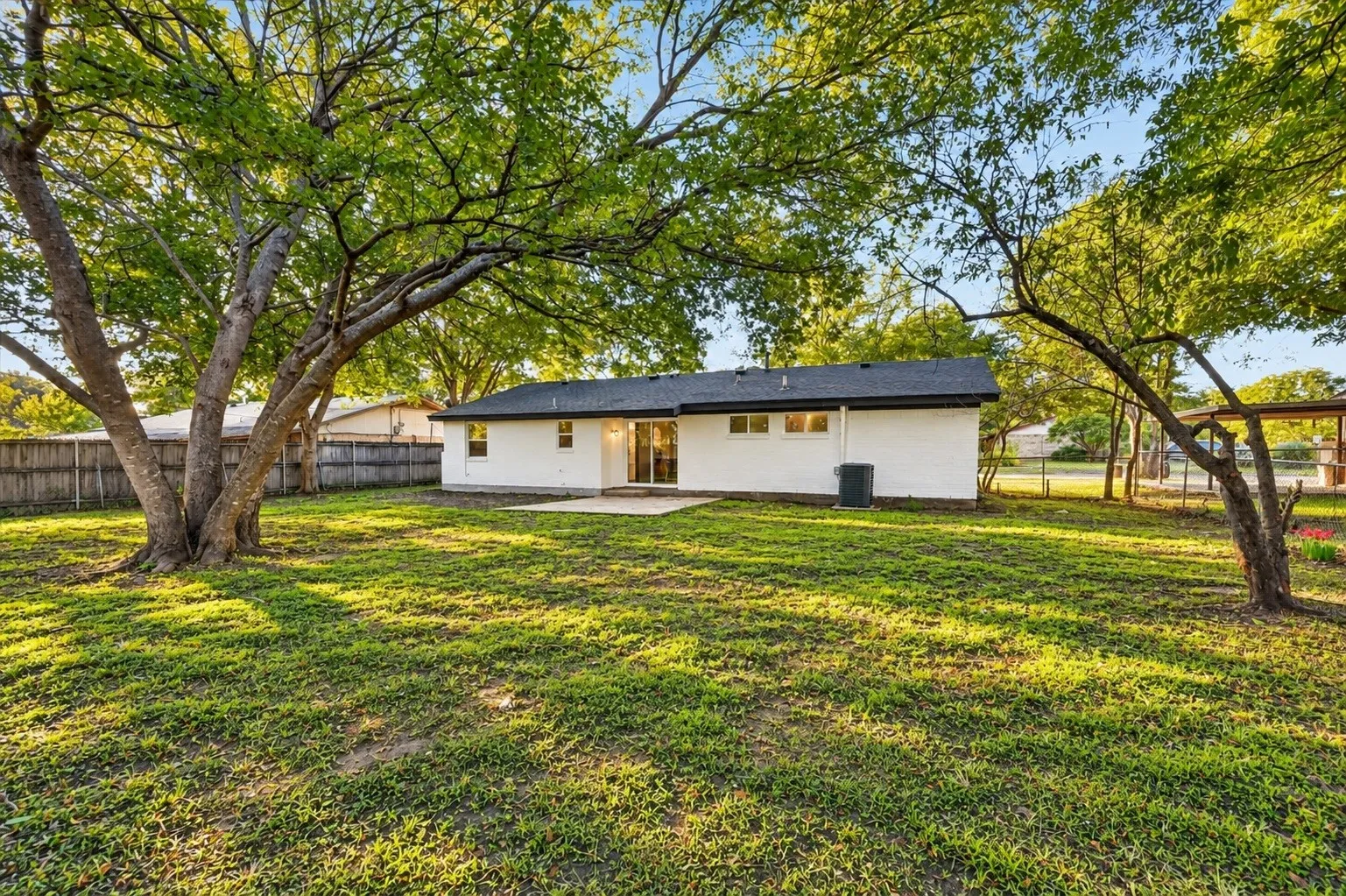 Expansive backyard featuring a lush lawn, mature trees, privacy fencing, and a concrete patio