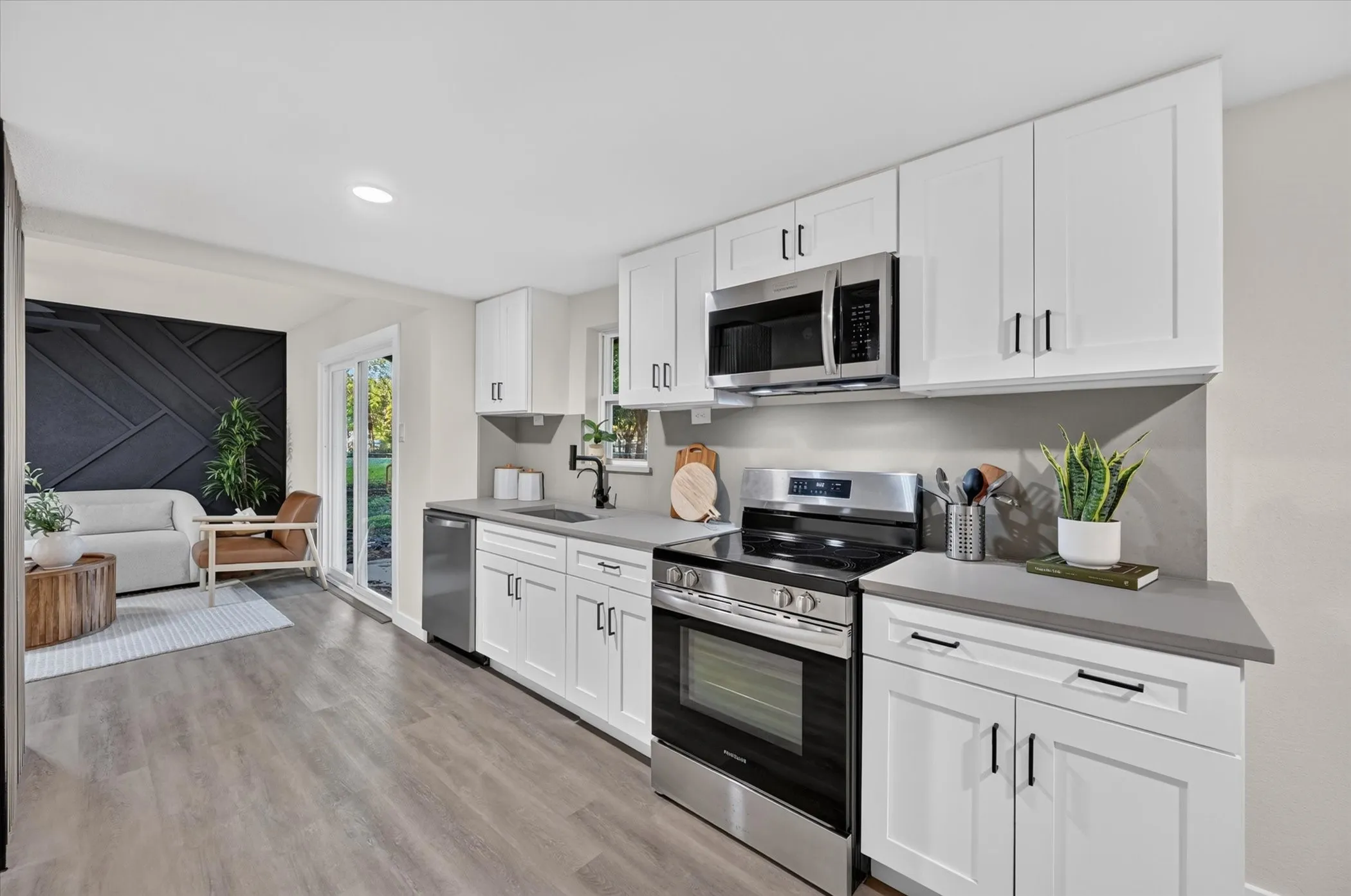Modern kitchen featuring white shaker cabinetry, stainless steel appliances, gray countertops, and wood-finish flooring