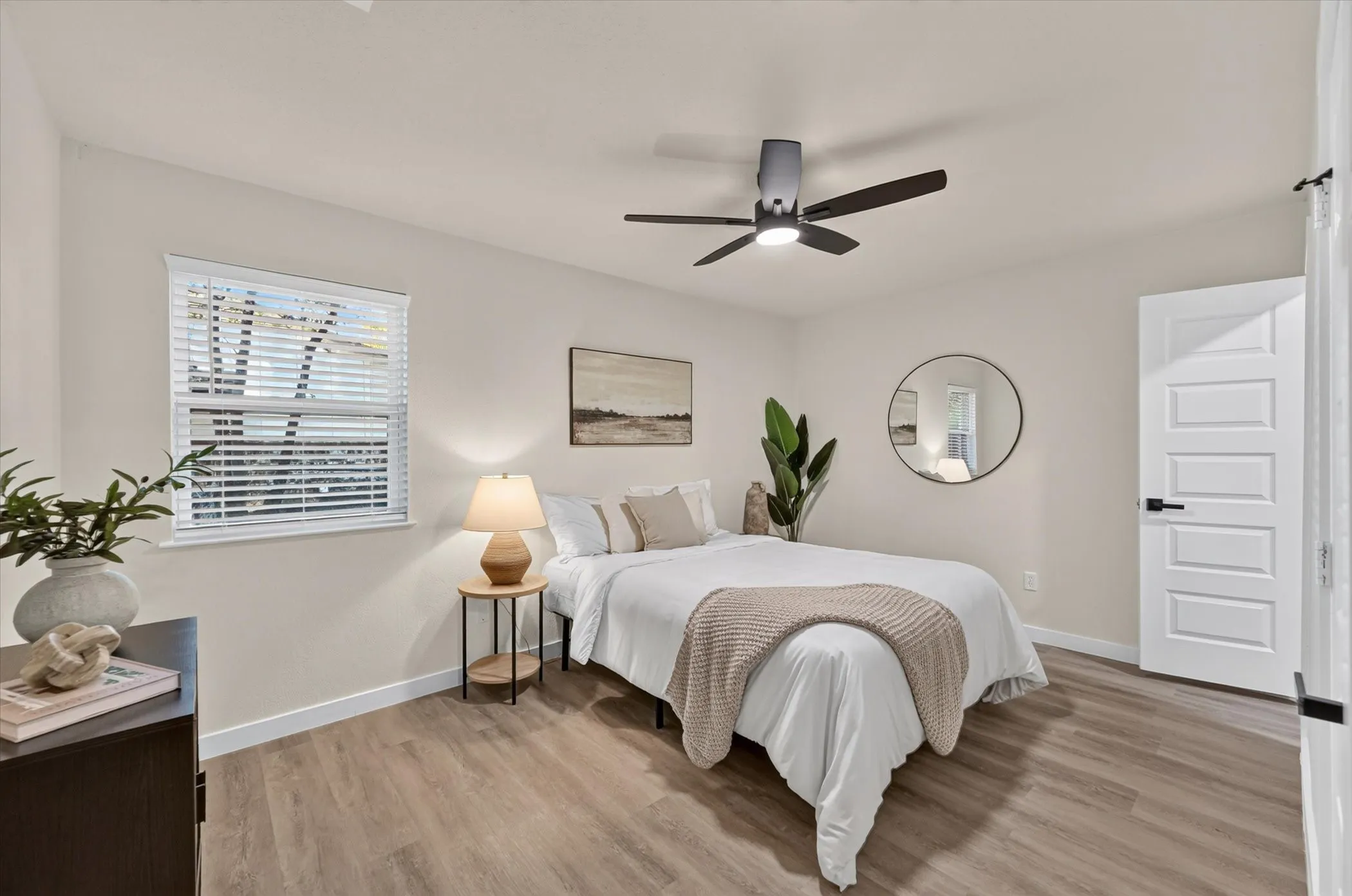 Neutral tone wall paint, wood-finish flooring, white window blinds, modern ceiling fan with integrated lighting, and a white paneled door with black hardware