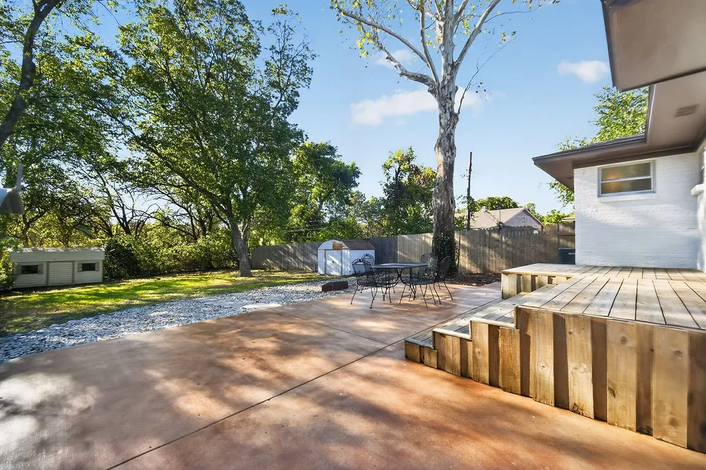 Outdoor living space featuring a wood-plank deck, concrete patio, gravel pathway, and mature trees