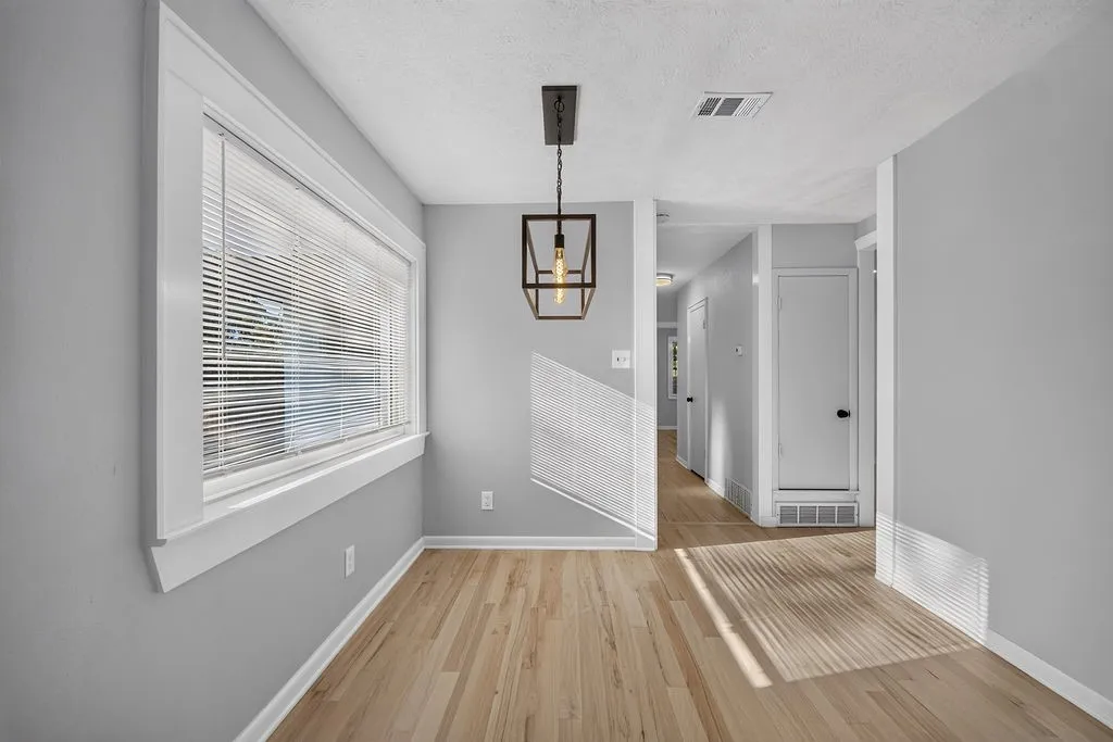 Full-height grey cabinetry with matte black hardware, stainless steel refrigerator, recessed lighting, wood-finish flooring, and a modern ceiling light fixture