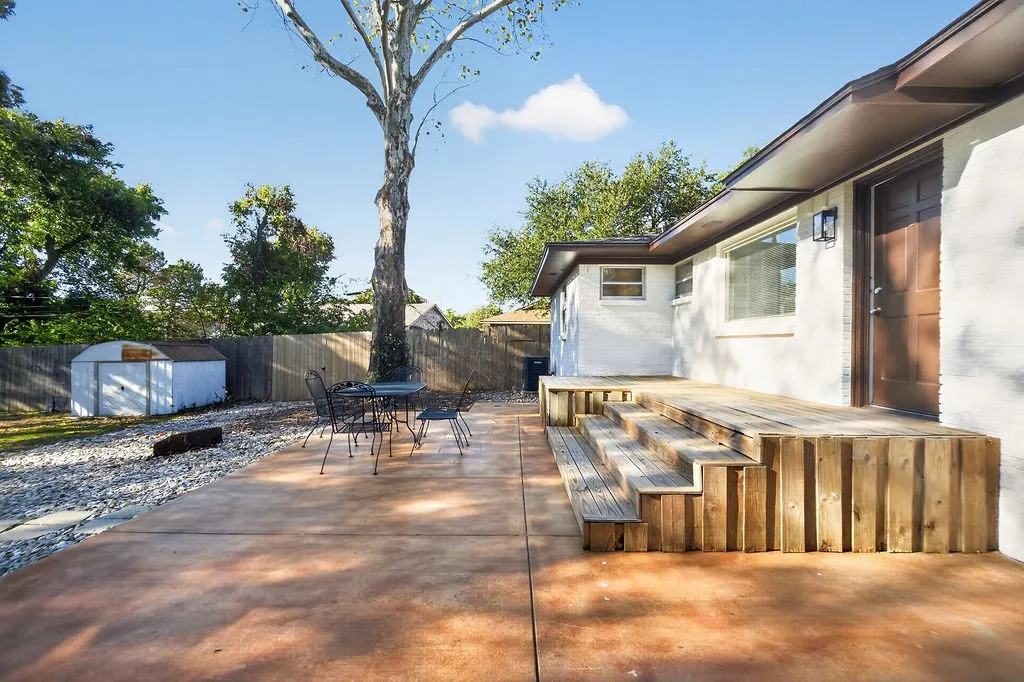 Expansive concrete patio with a tiered wood deck, privacy fencing, and exterior storage shed