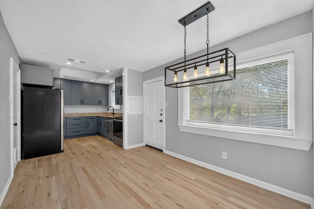 Wood-finish flooring, modern linear chandelier, gray wall paint, white trim, and a kitchen featuring blue cabinetry and light-colored countertops