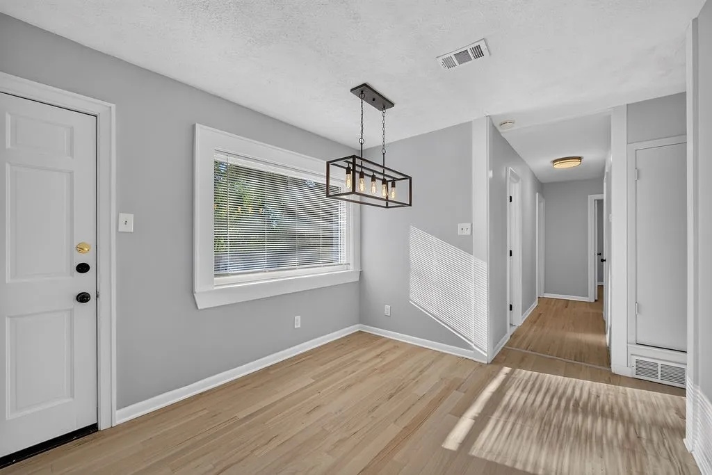 Light wood-finish flooring, a contemporary black metal chandelier, and a white paneled door