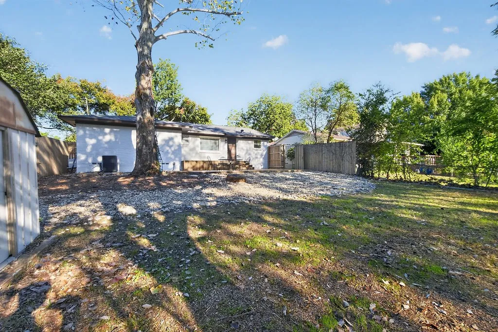 Expansive backyard featuring a large mature tree, gravel landscaping, and a wooden privacy fence