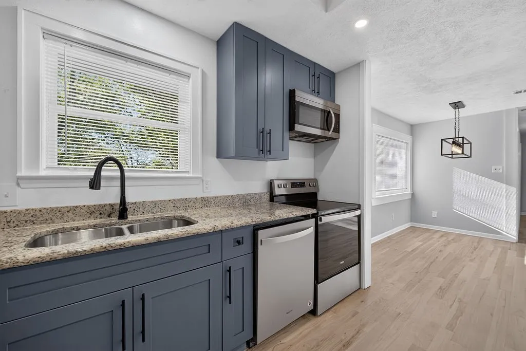 Kitchen featuring blue shaker cabinetry, granite-style countertops, stainless steel appliances, and a double basin sink with a matte black faucet