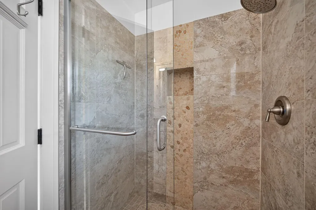 Glass-enclosed shower featuring natural stone-finish tiling, a built-in shower niche, and a rain showerhead