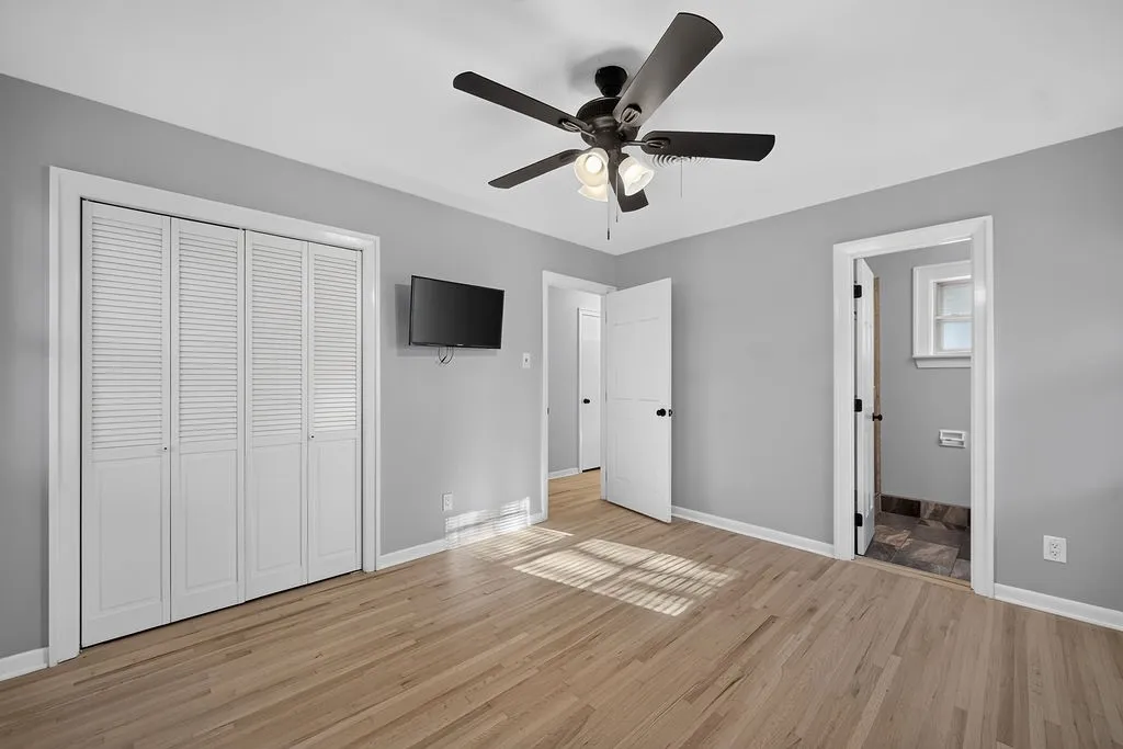 Light wood-finish flooring, white louvered bifold closet doors, ceiling fan with integrated lighting, and gray wall paint
