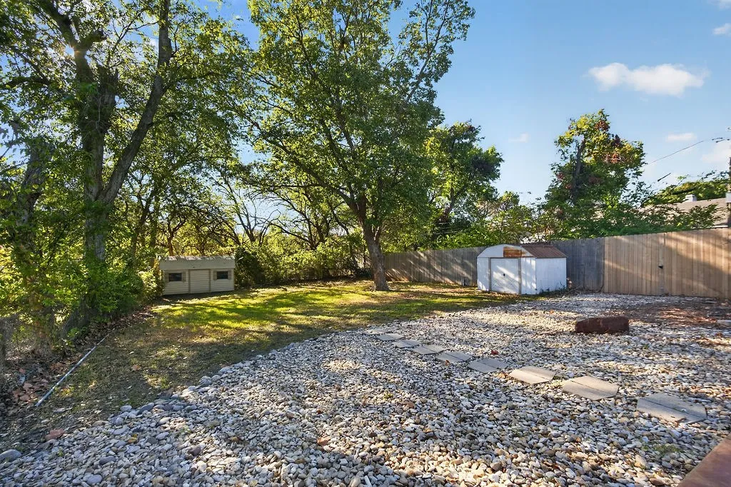 Expansive backyard featuring a gravel patio with stepping stones, a wooden privacy fence, mature trees, and a storage shed