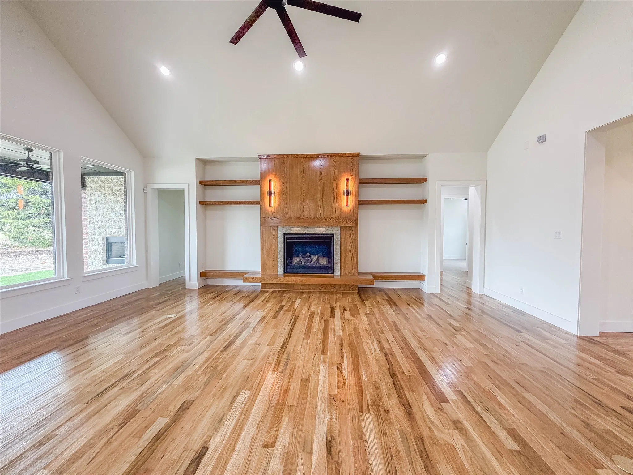 Vaulted ceilings with recessed lighting, wood-finish flooring, a built-in fireplace with a wood-finish mantel and integrated shelving, and large windows