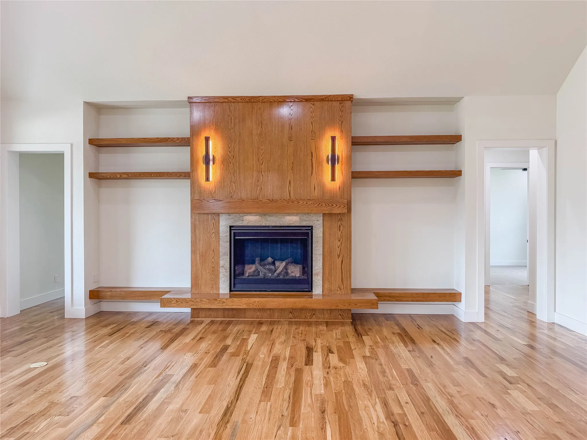 Hardwood flooring, built-in shelving, stone fireplace surround, wood fireplace mantle, and integrated wall sconces