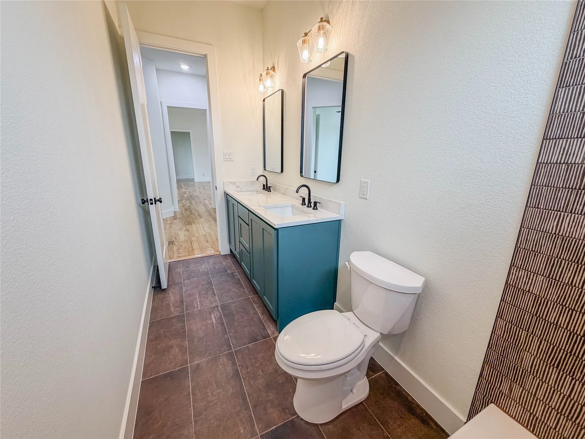 Walk-in shower with clear glass enclosure and black hardware, patterned floor tile, single vanity with dark countertop, and rectangular undermount sink