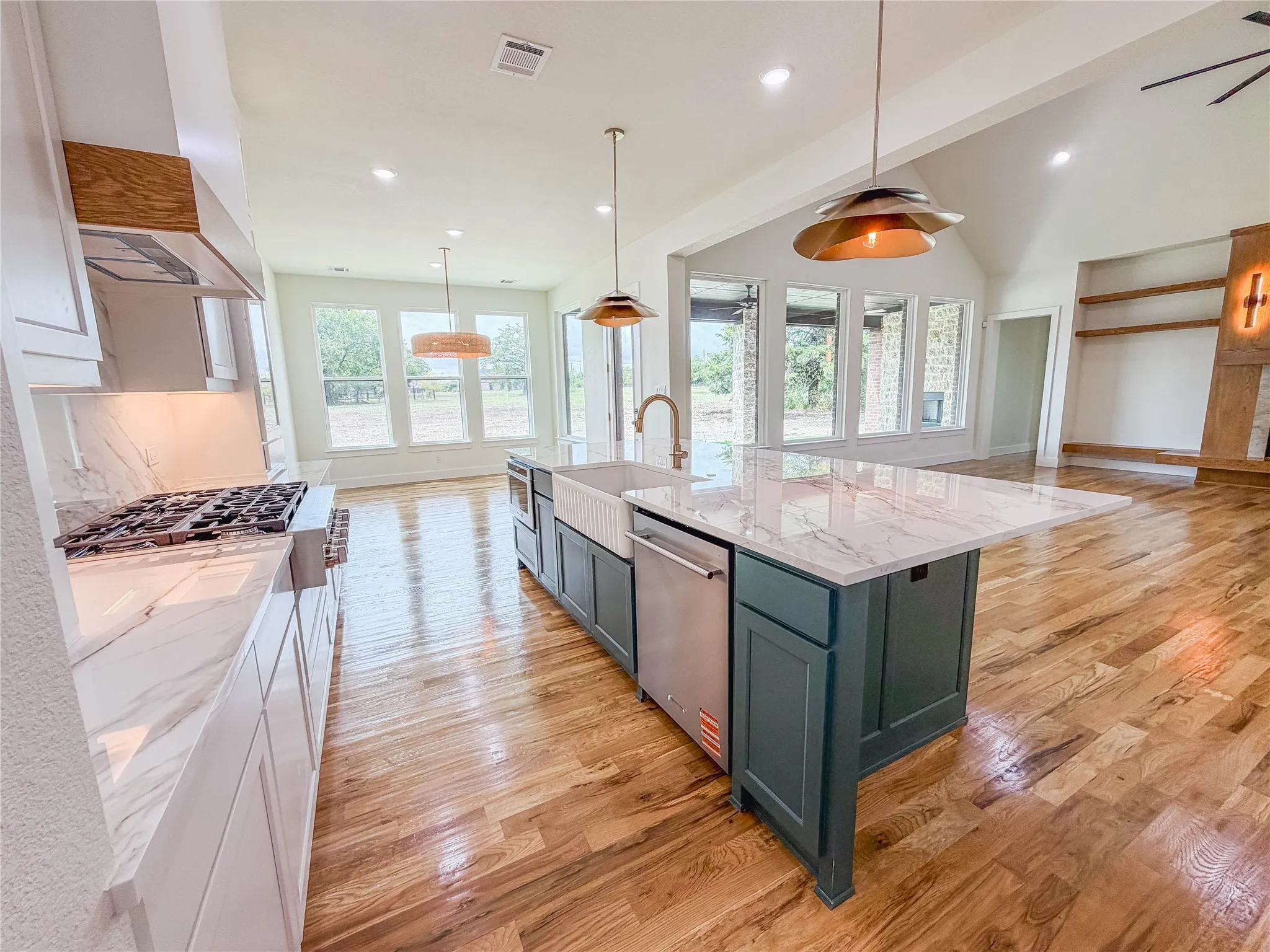 Open-concept kitchen with a large island featuring a farmhouse sink, stainless steel appliances, marble-look countertops, and wood-finish flooring
