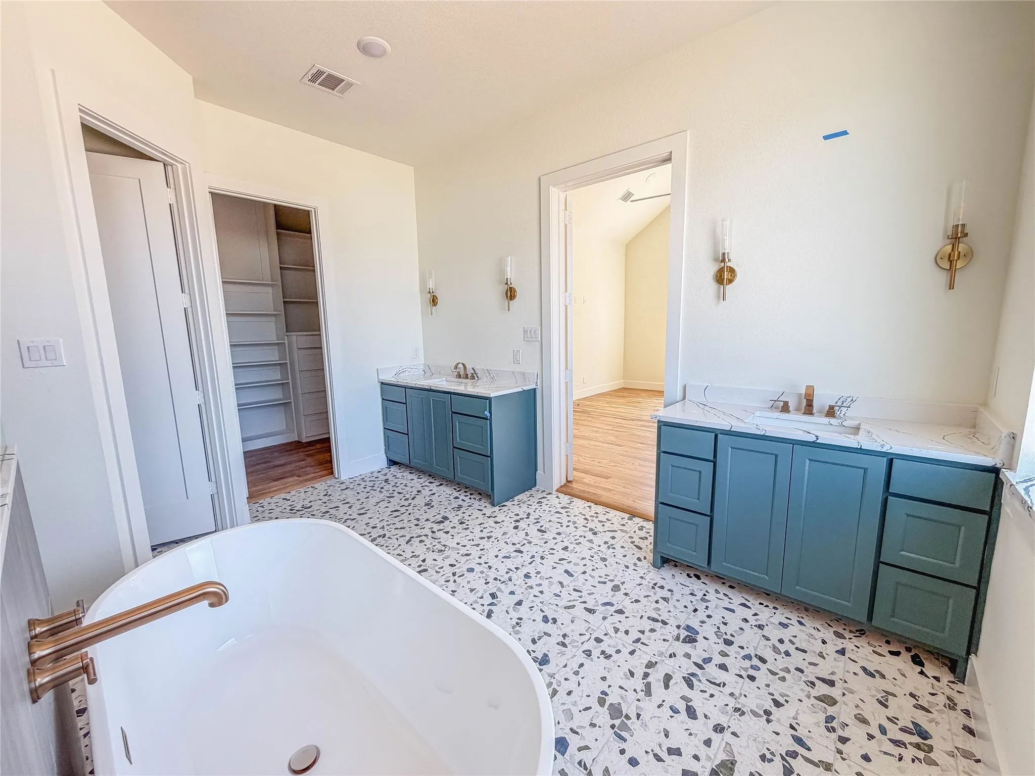 Freestanding soaking tub with a bronze-finish faucet, dual vanity sinks with light-toned countertops, and built-in closet shelving