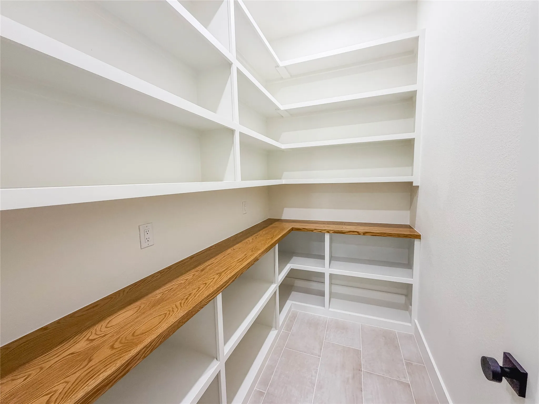 Built-in shelving with white finishes, wood-finish countertop, and light-toned tile flooring