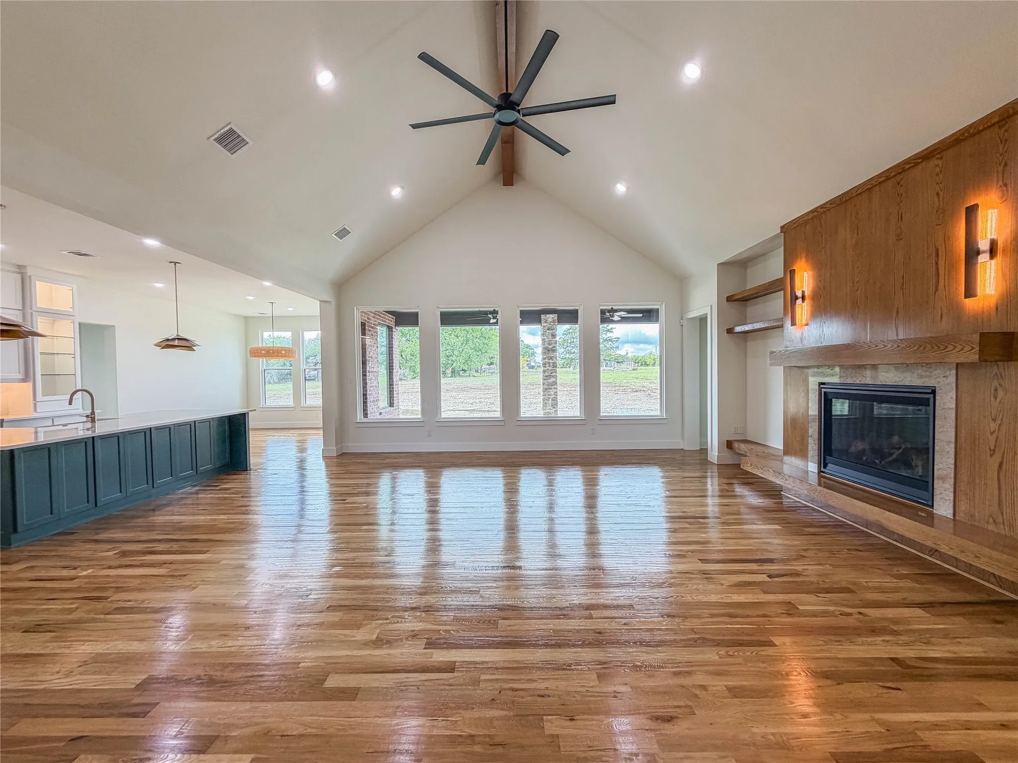 Vaulted ceilings with exposed beam, wood-finish flooring, built-in fireplace with wood mantel, large island with integrated sink, and recessed lighting