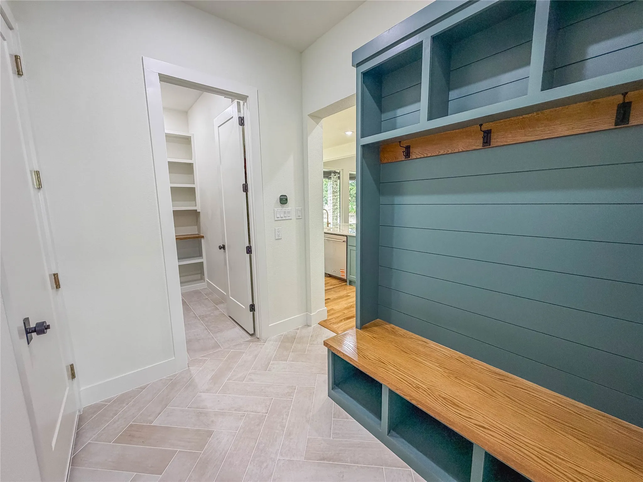 Herringbone tile flooring, built-in storage bench with wood top, teal shiplap detailing, overhead shelving, and a dedicated pantry