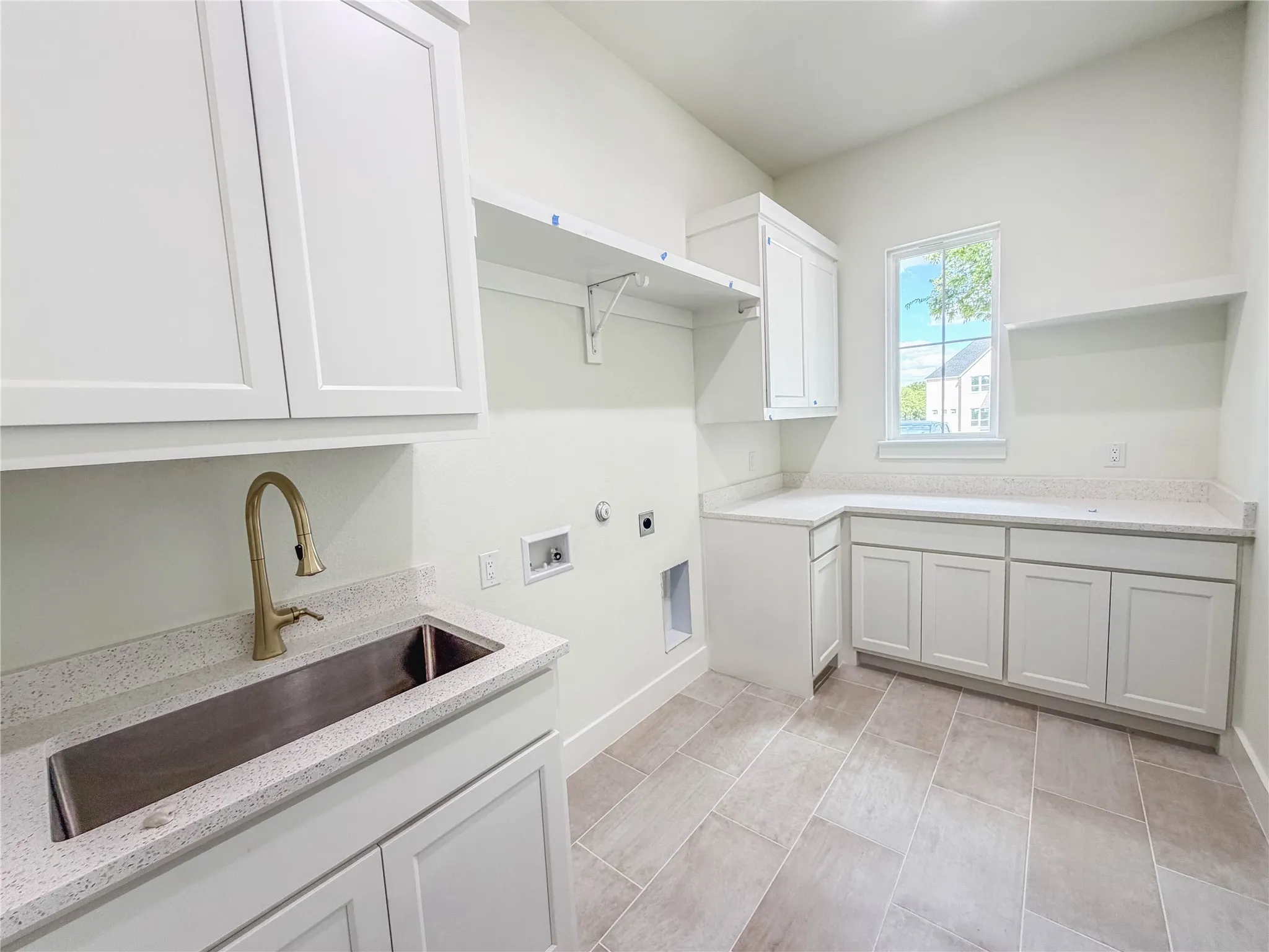 White cabinetry with ample storage, integrated stainless steel sink, gold-finish faucet, light-toned countertops, and tile flooring