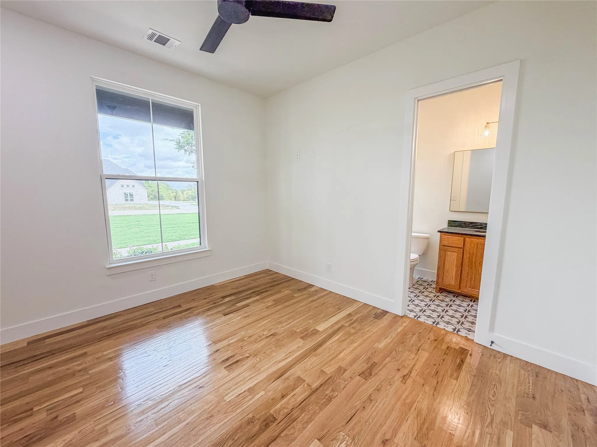 Wood flooring, ceiling fan, single window, bathroom access, white walls