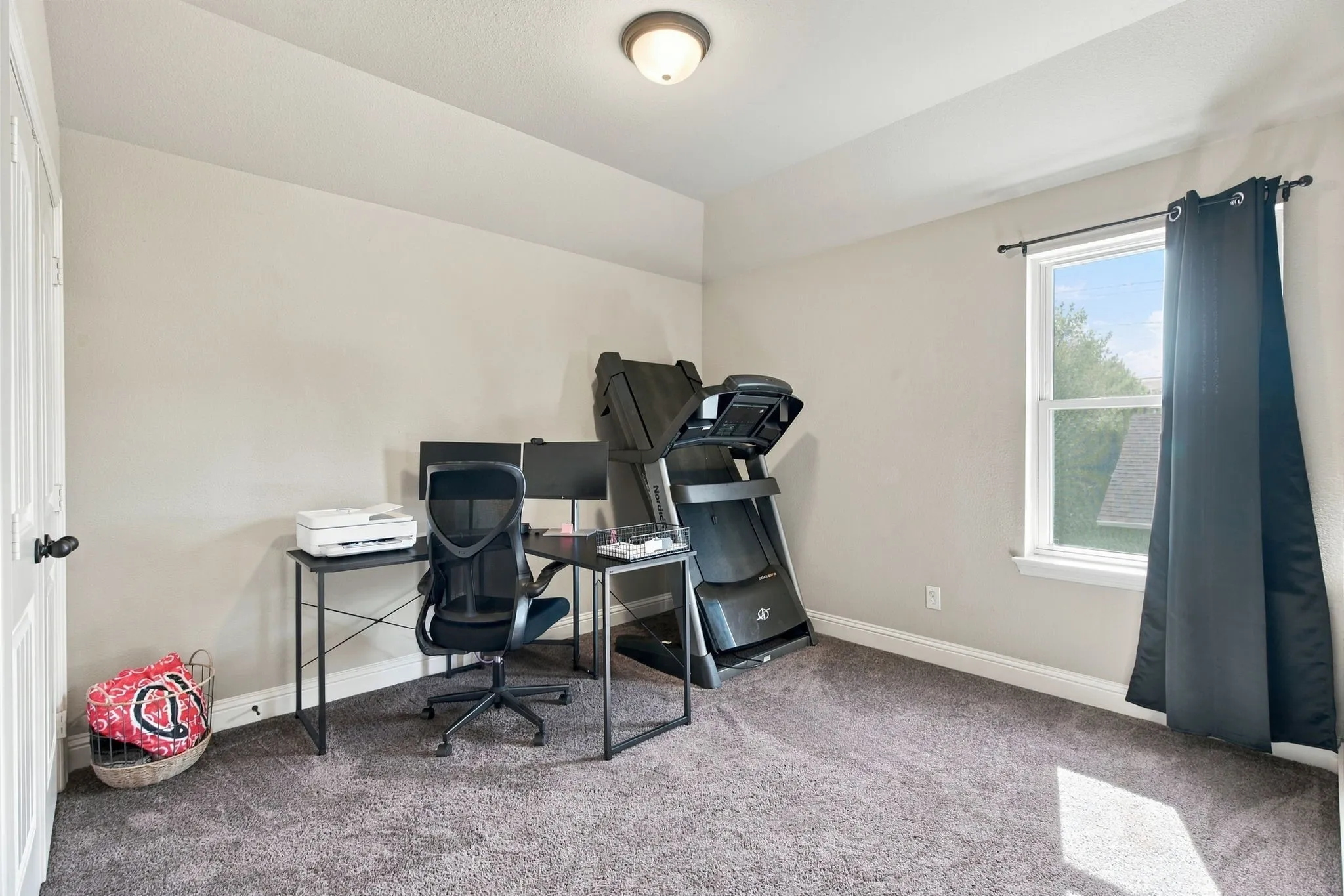 Versatile upstairs bedroom currently used as a home office and exercise space, featuring a large window, ceiling fan, and flexible floor space.