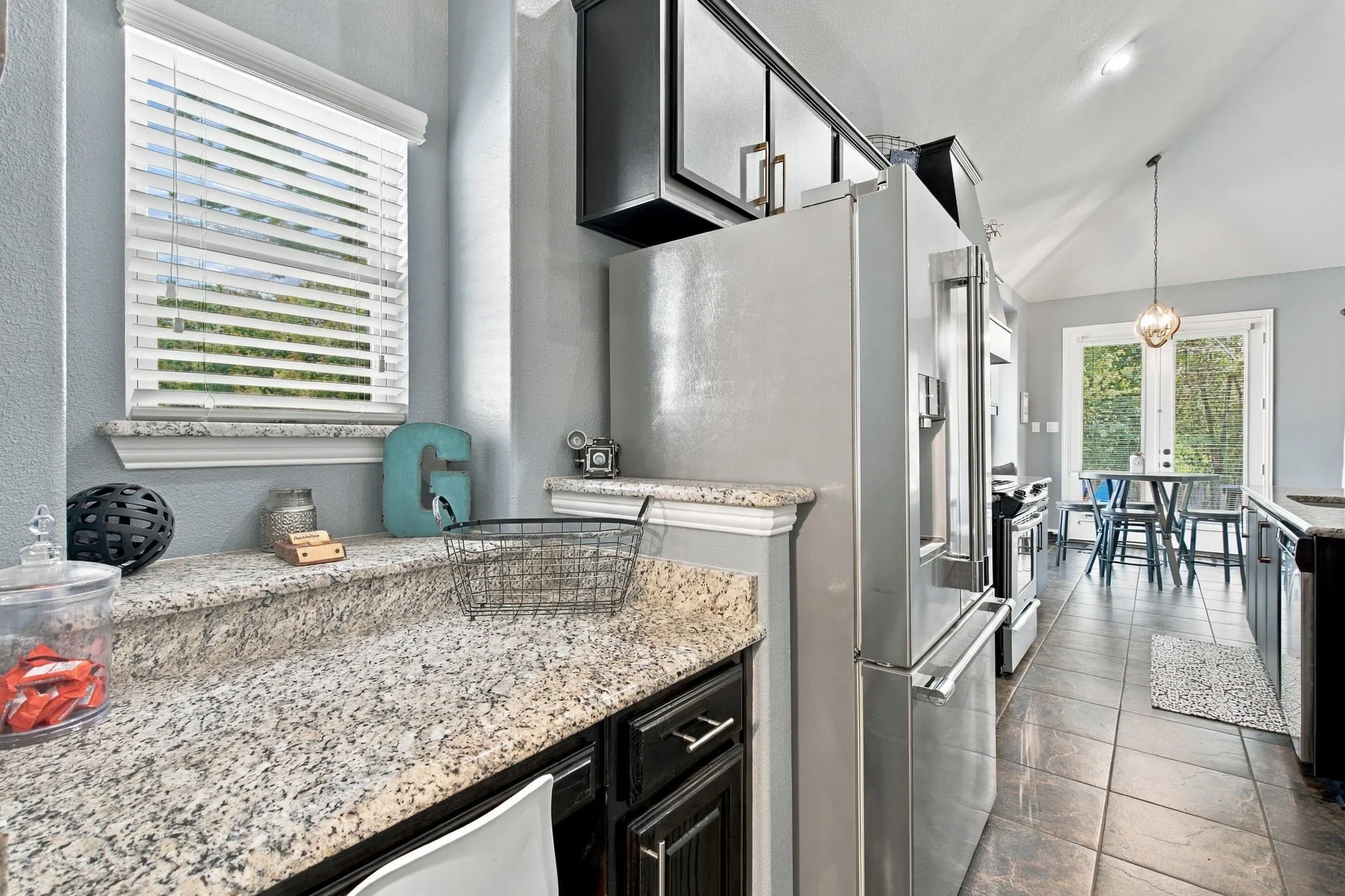 Additional counter and cabinet space beside the stainless steel refrigerator provides convenient storage and prep space that can serve as a butler's pantry or sitting desk, with a nearby breakfast nook overlooking the backyard.
