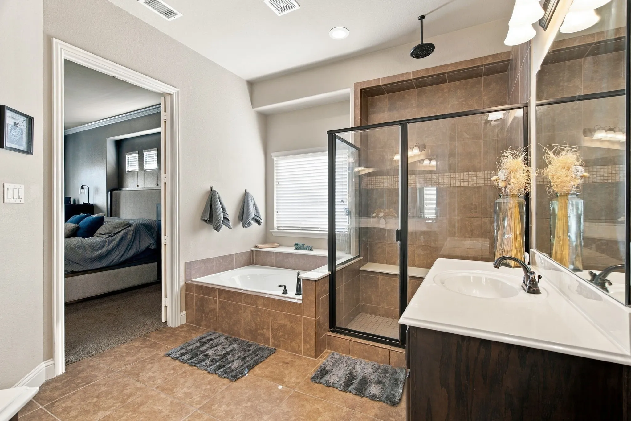 Primary ensuite bathroom with a separate soaking tub beneath a window, an oversized tiled walk-in shower with glass enclosure, and a spacious vanity area.