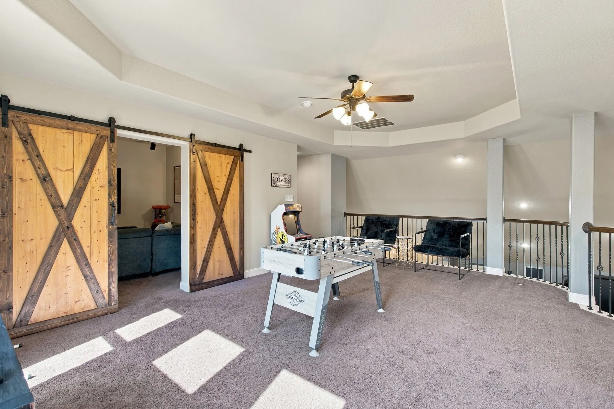 Generously sized entertainment space featuring natural light, plush carpeting, and rustic sliding barn doors leading into the adjoining media room.