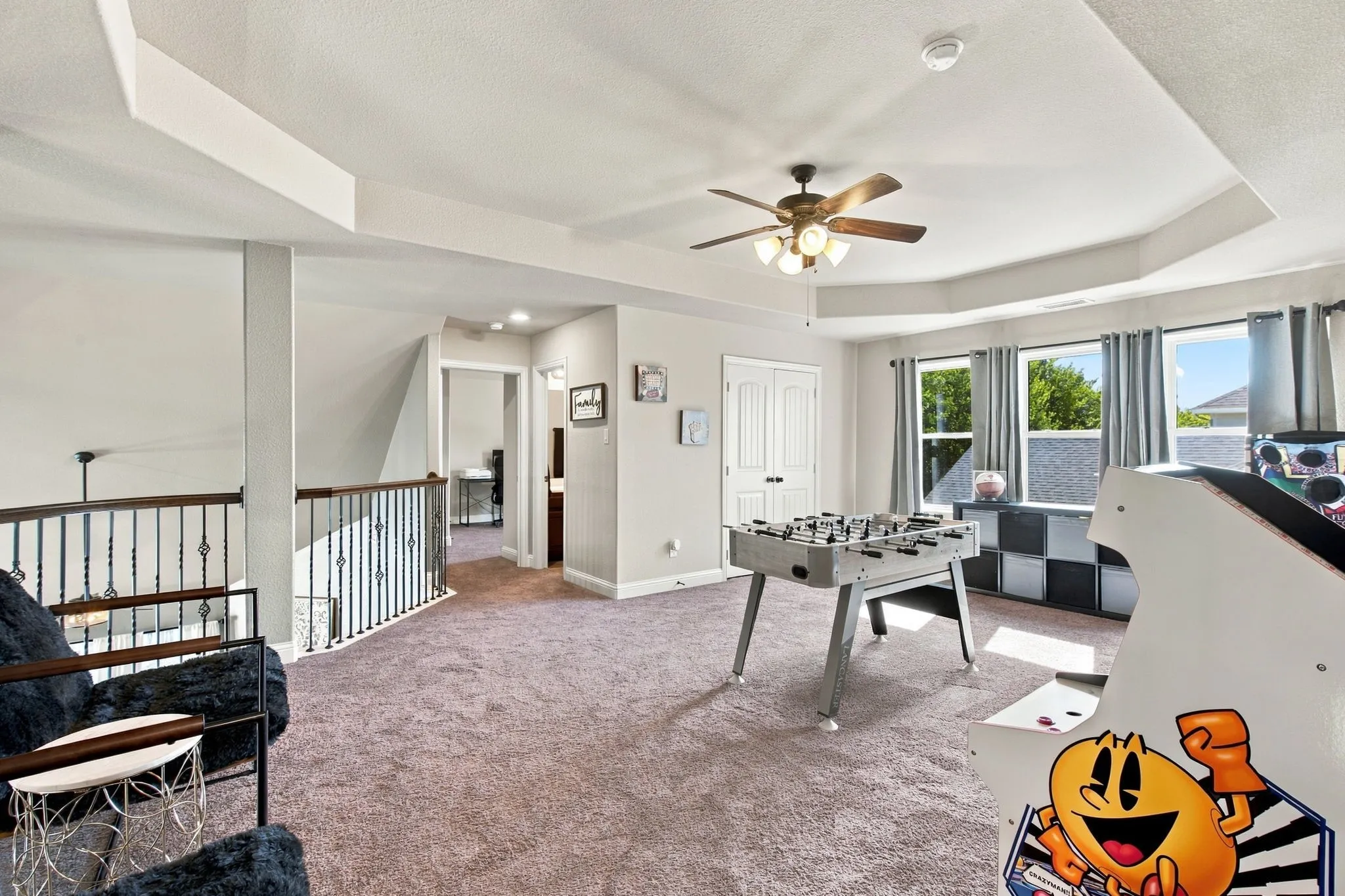 Open upstairs gathering area overlooking the main level, with decorative iron railings, abundant floor space, and access to the media room through sliding barn doors.