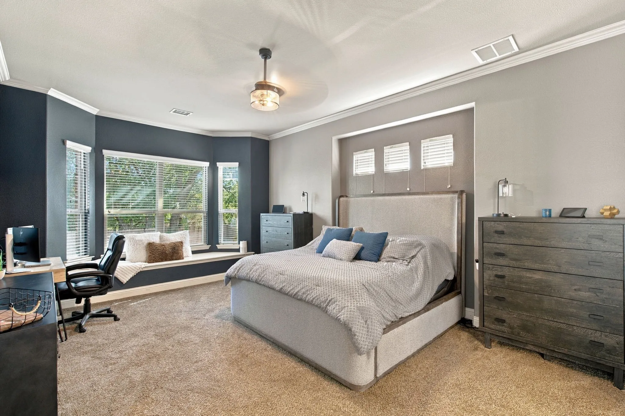 Spacious downstairs primary suite featuring a large bay window with built-in window seating, crown molding, and plenty of room for a king-sized bed and additional furnishings.