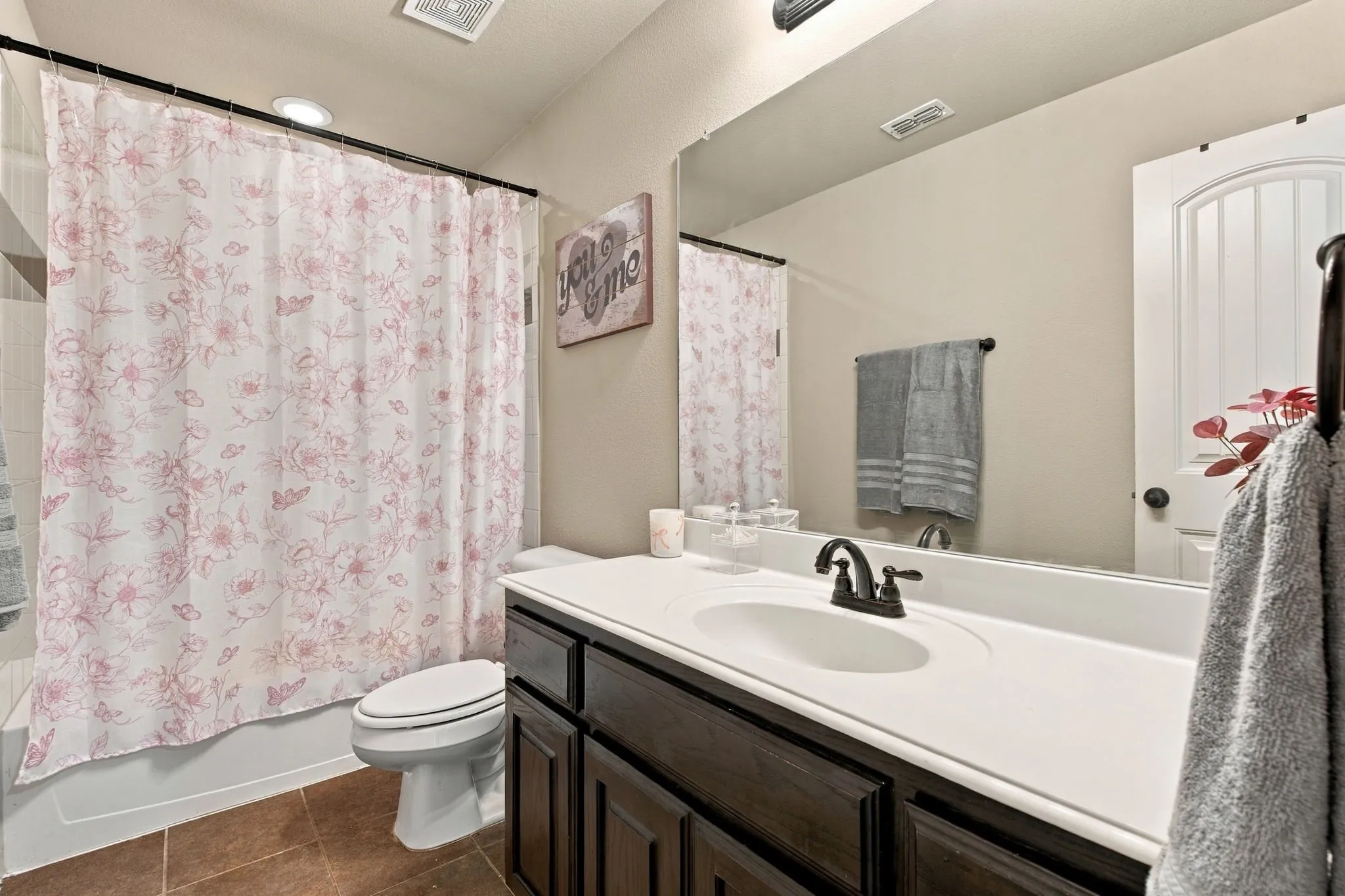 Upstairs full bathroom featuring a tub-shower combination, dark wood vanity, generous countertop space, and a large wall mirror.