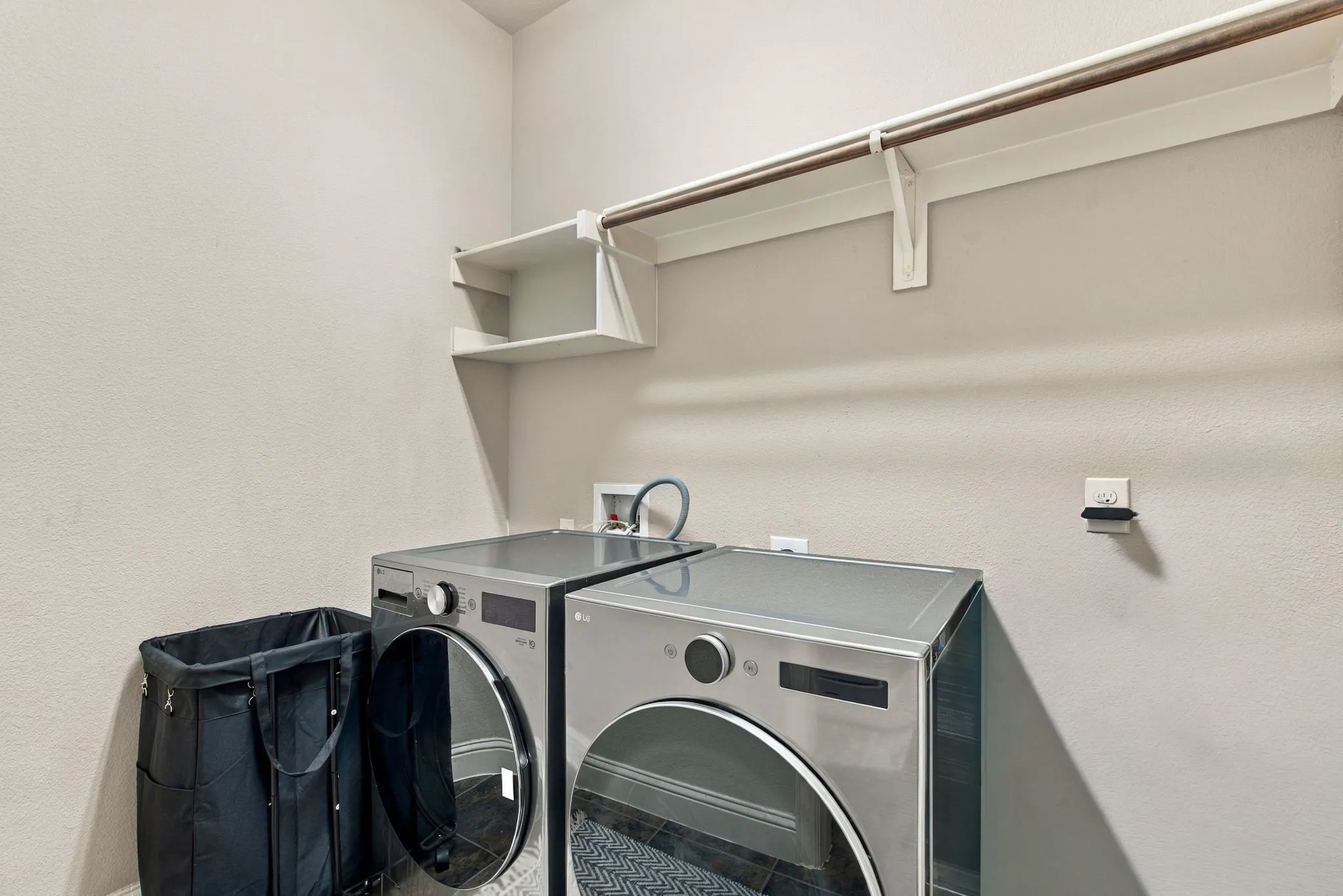 Dedicated spacious laundry room with full-size washer and dryer, overhead shelving, and hanging space for added convenience.