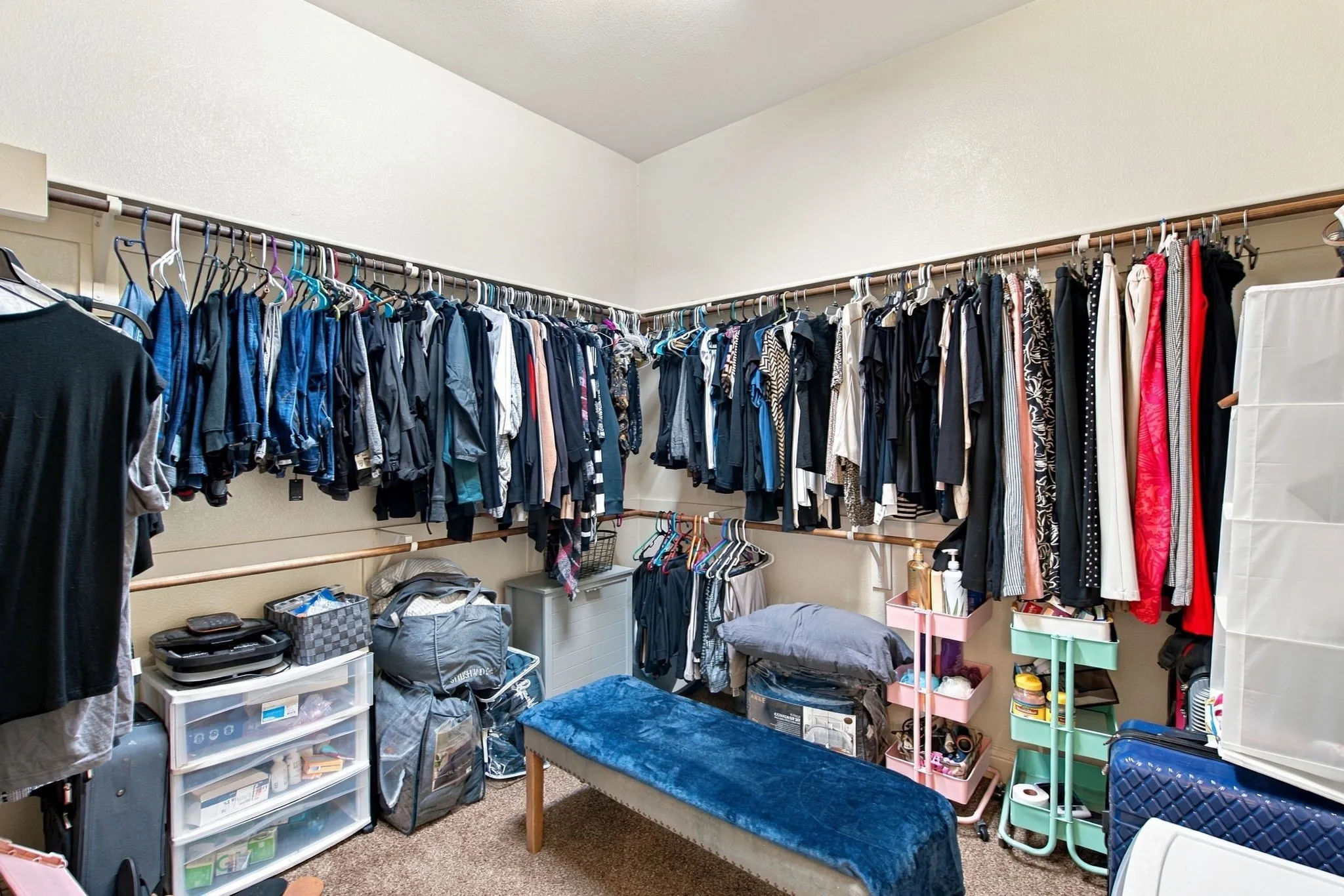 Spacious primary walk-in closet with hanging rods along three walls, multiple storage levels, and ample room for clothing and accessories.