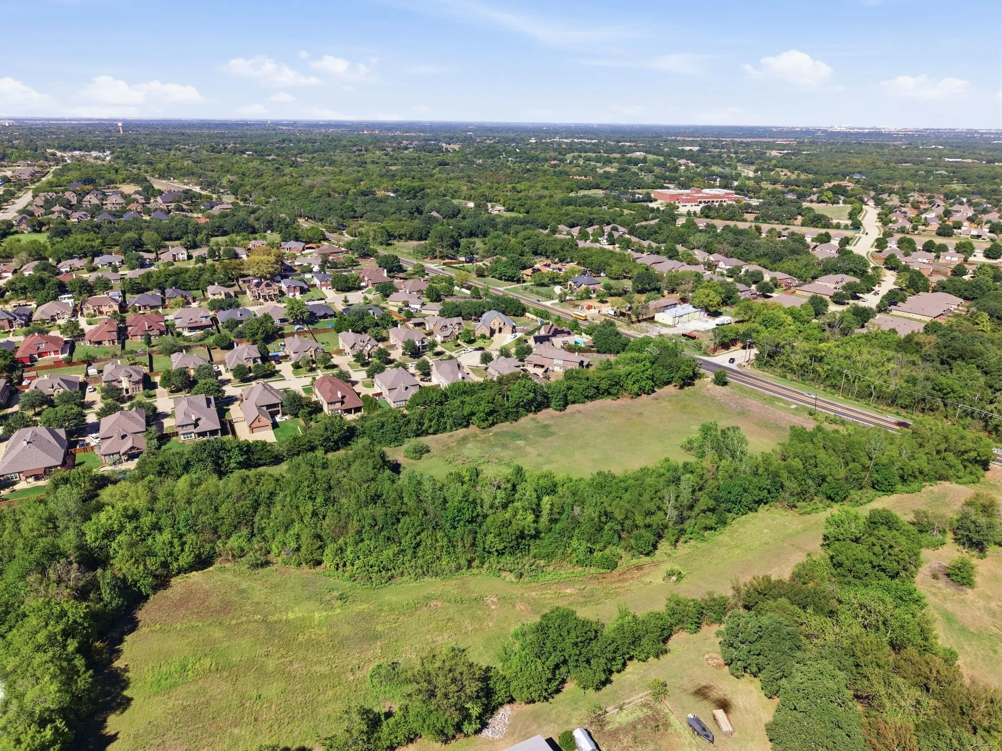 Aerial perspective highlighting the established neighborhood, spacious surroundings, and dense tree coverage behind the homes.