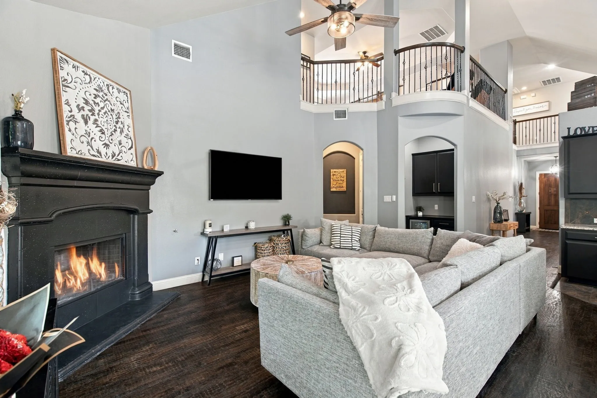 Spacious living area centered around a statement fireplace with a dark mantel, complemented by soaring ceilings and an open view of the upstairs balcony.