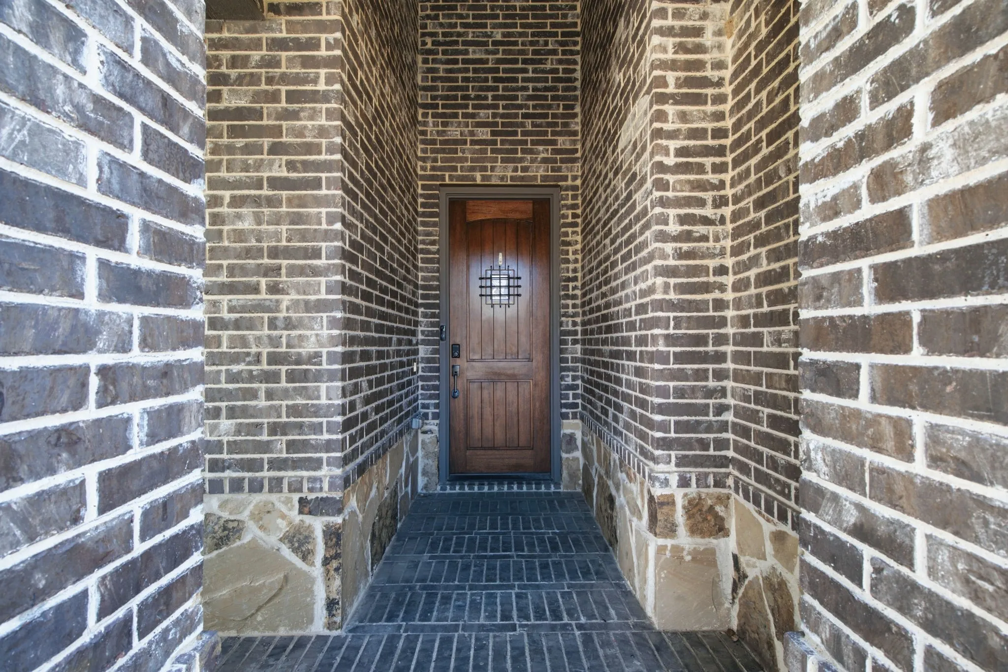 Recessed entryway featuring rich brick and stone detailing, brick paver flooring, and a handsome wood front door.