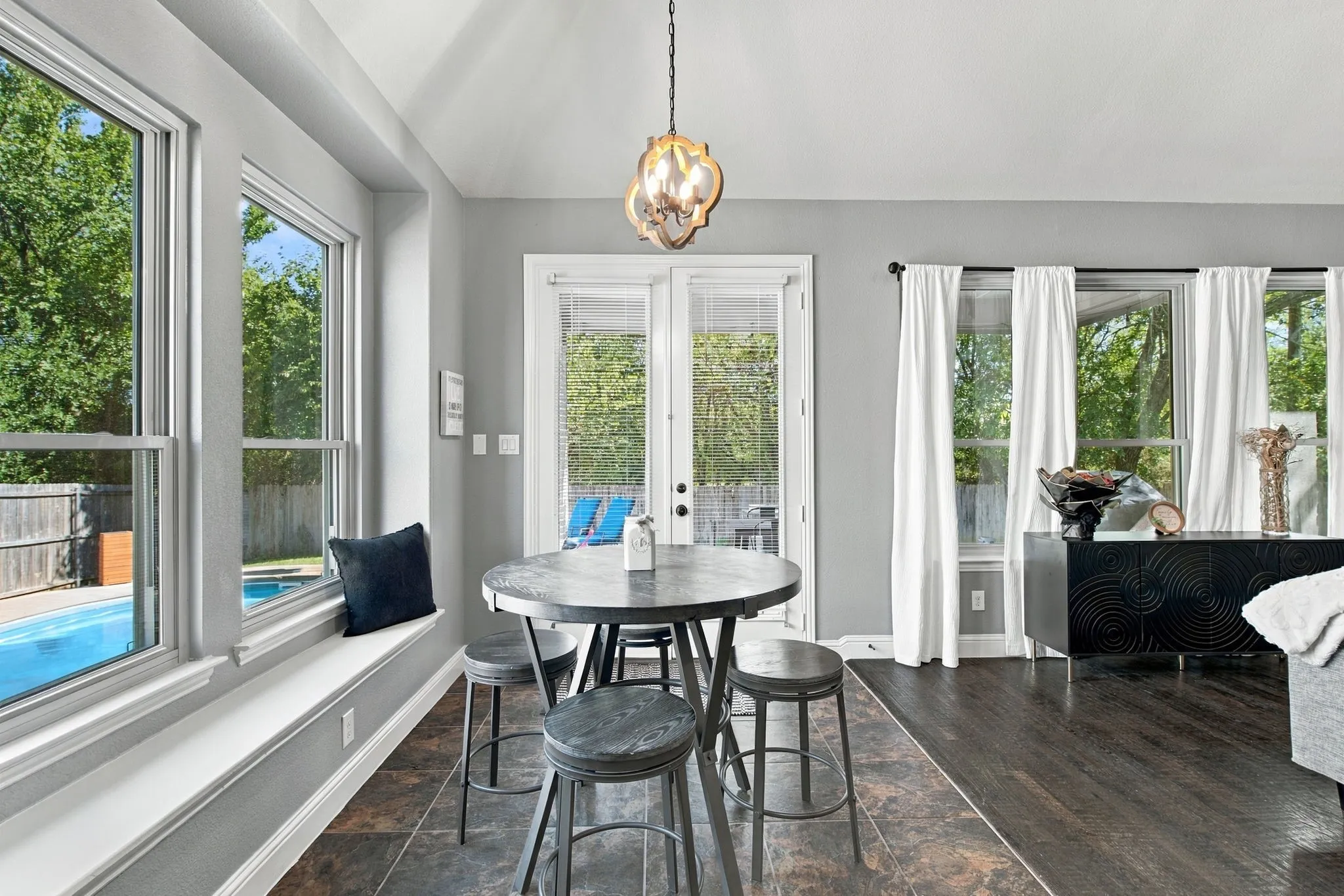 Bright breakfast area featuring a charming window seat, decorative pendant lighting, and French doors opening toward the backyard and pool.