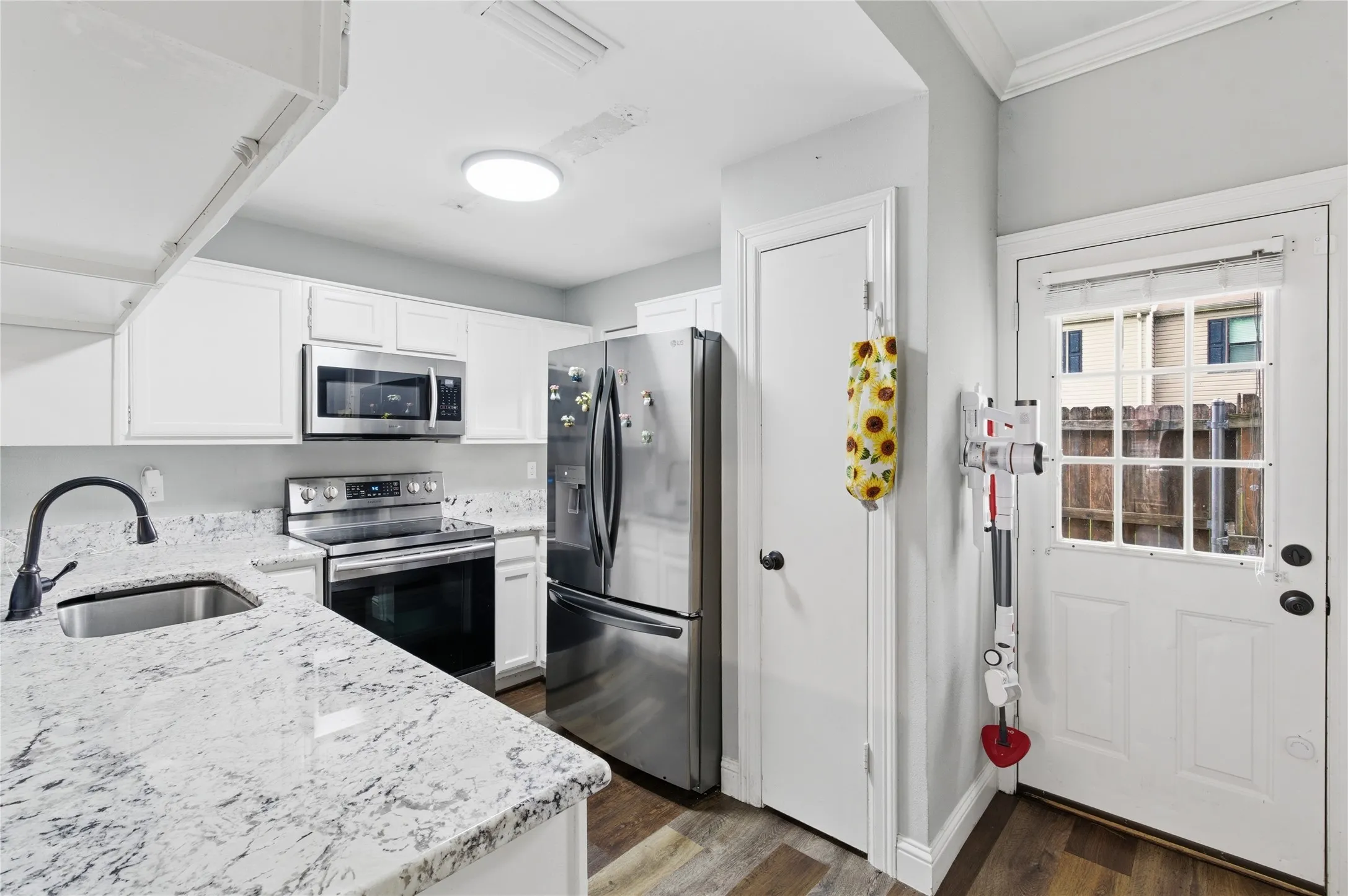 Kitchen featuring white cabinetry, stainless steel appliances, speckled countertops, a stainless steel sink with a matte black faucet, and wood-finish flooring