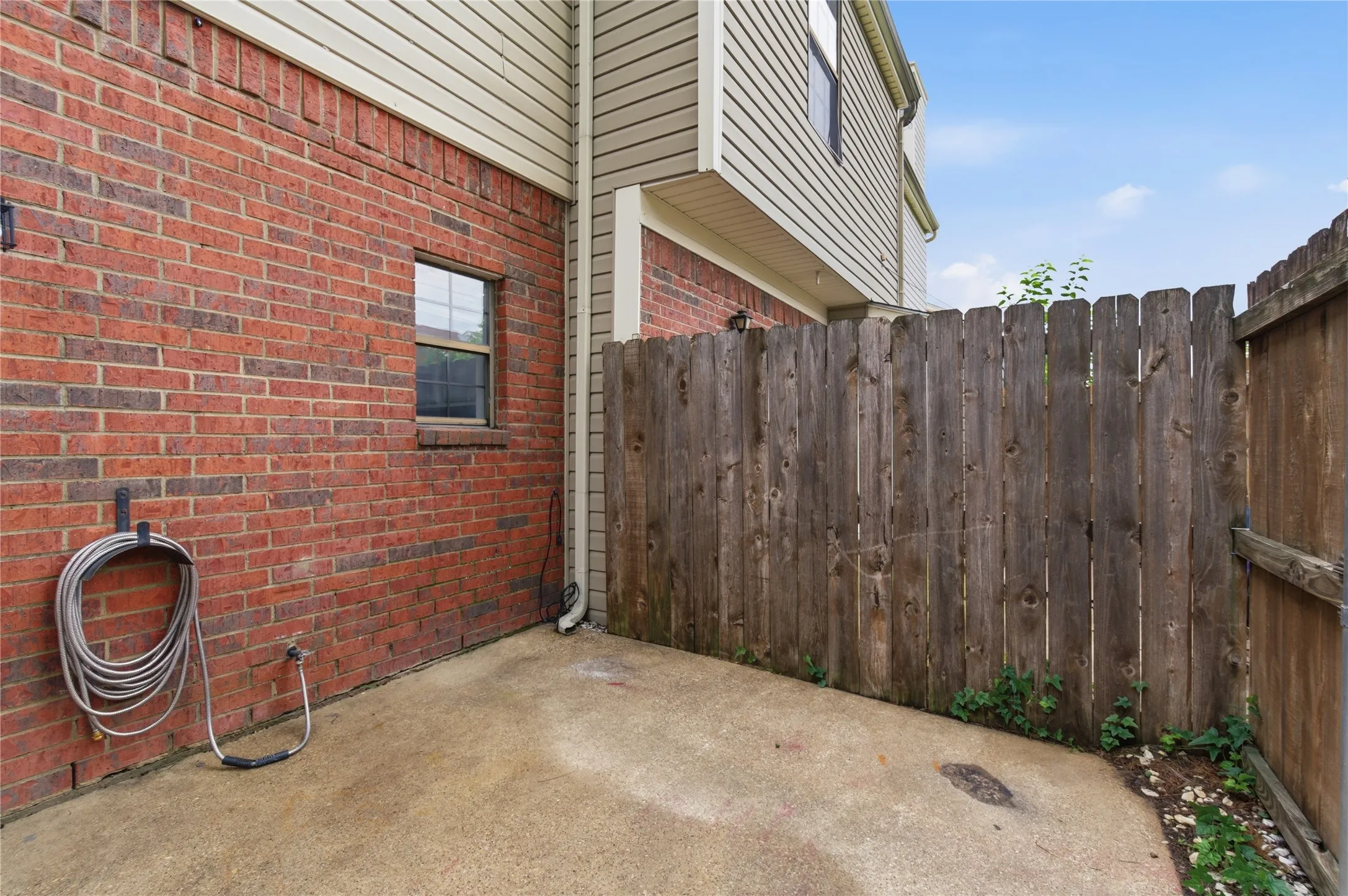 Brick exterior with siding, privacy fencing, and concrete patio