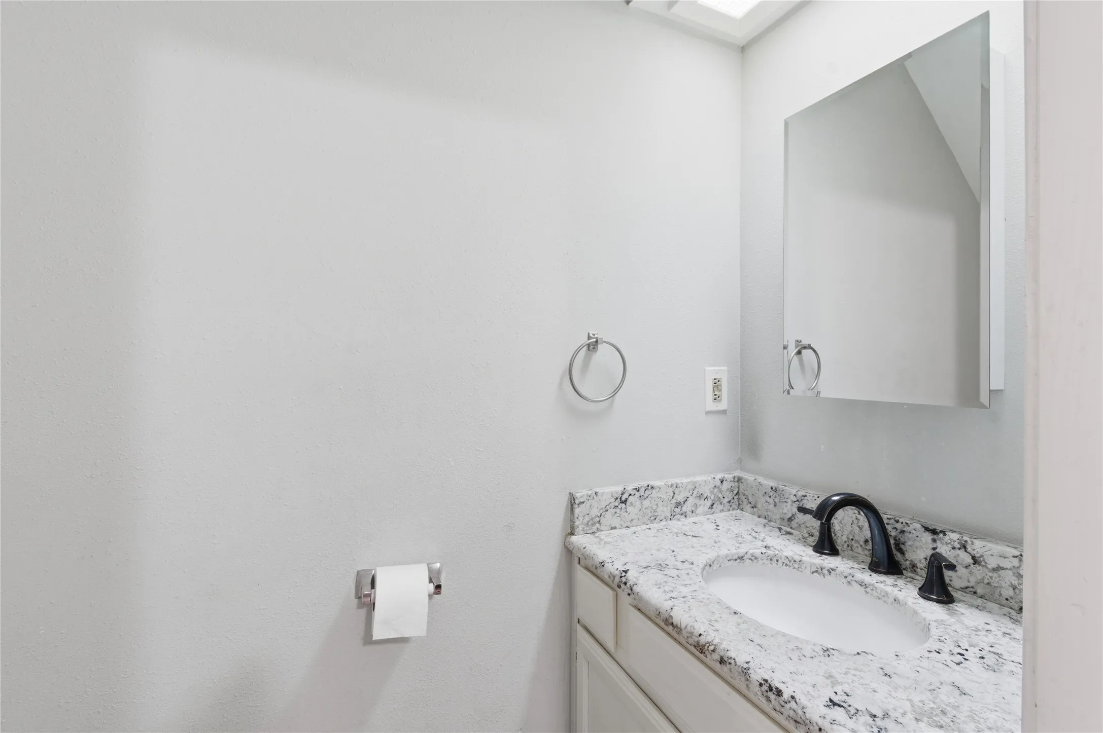 White vanity with a speckled countertop, undermount sink, black faucet, and a wall-mounted medicine cabinet