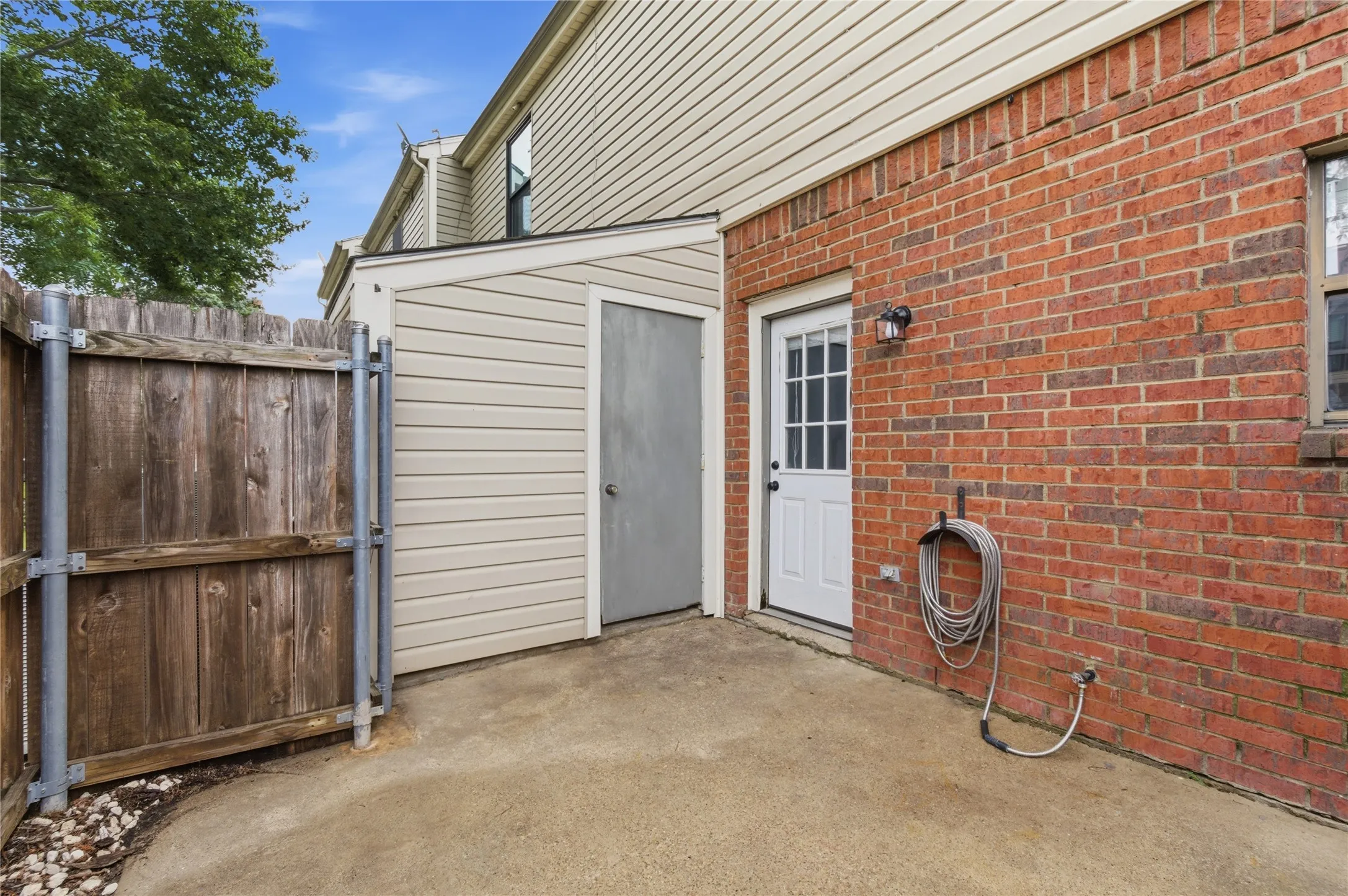 Brick exterior with white door, concrete patio, wood fence, and attached storage shed