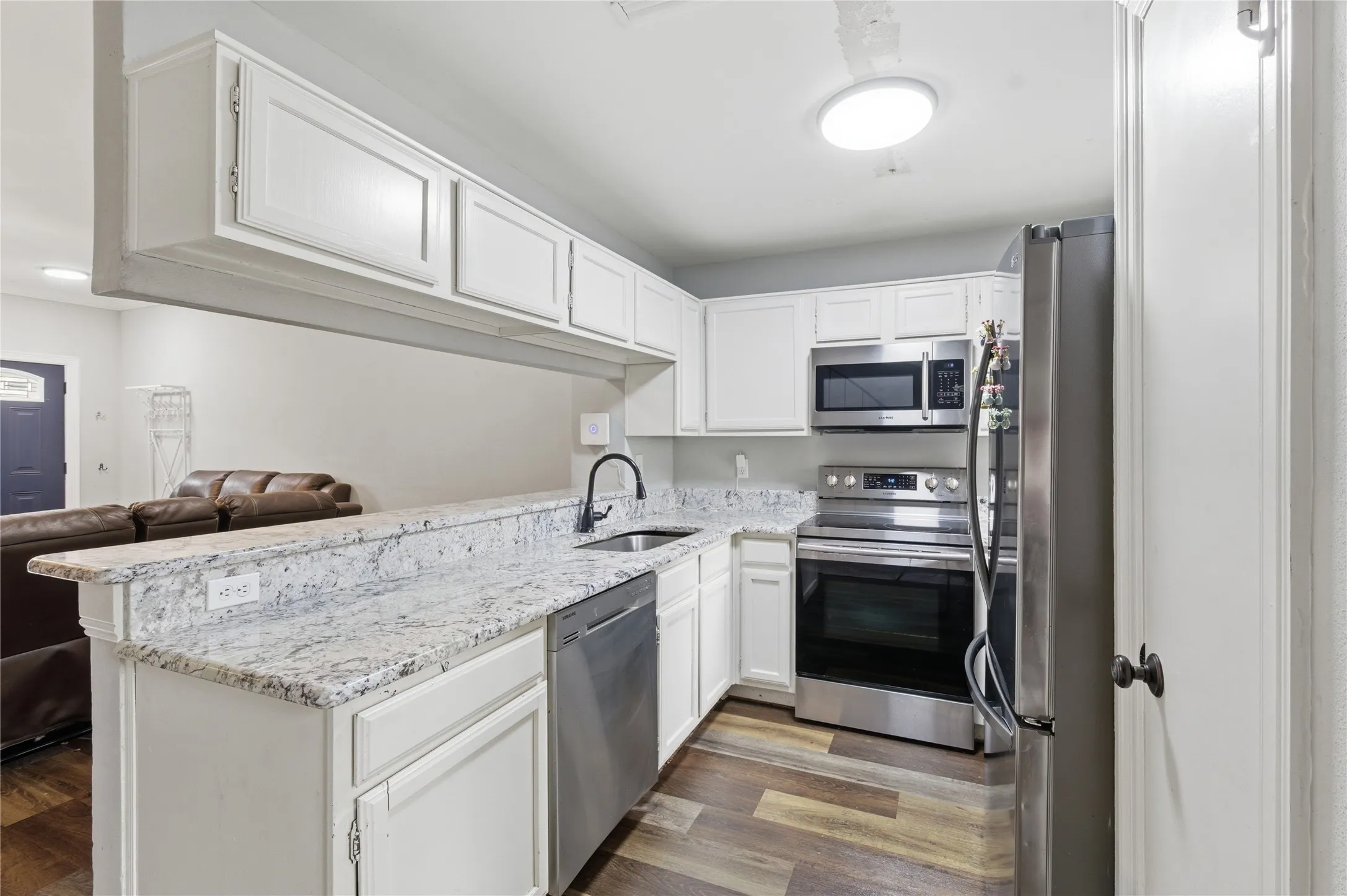 Bright kitchen featuring white cabinetry, light-toned countertops, stainless steel appliances, and wood-finish flooring