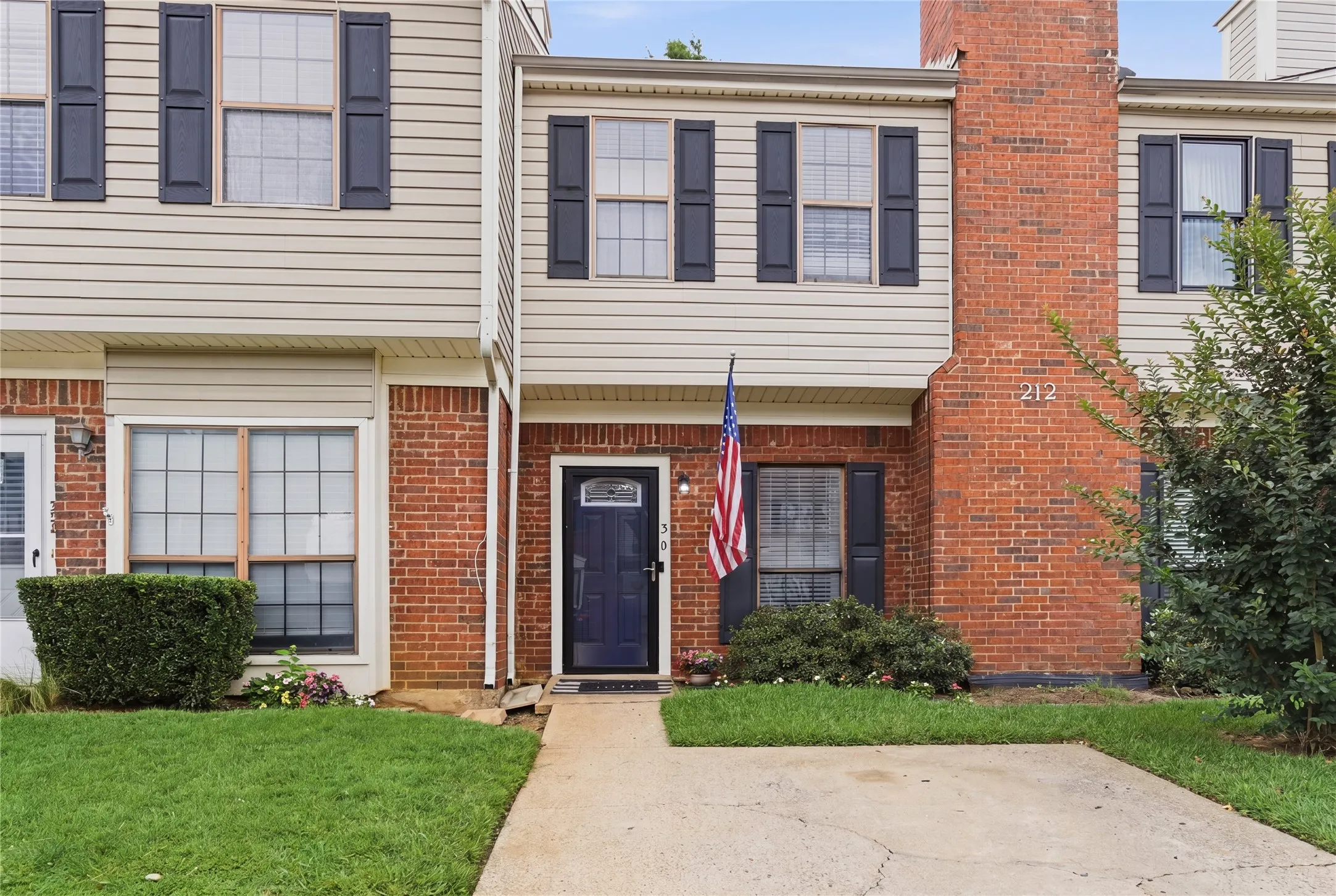 Brick and siding exterior with dark shutters, paved entryway, and established front landscaping