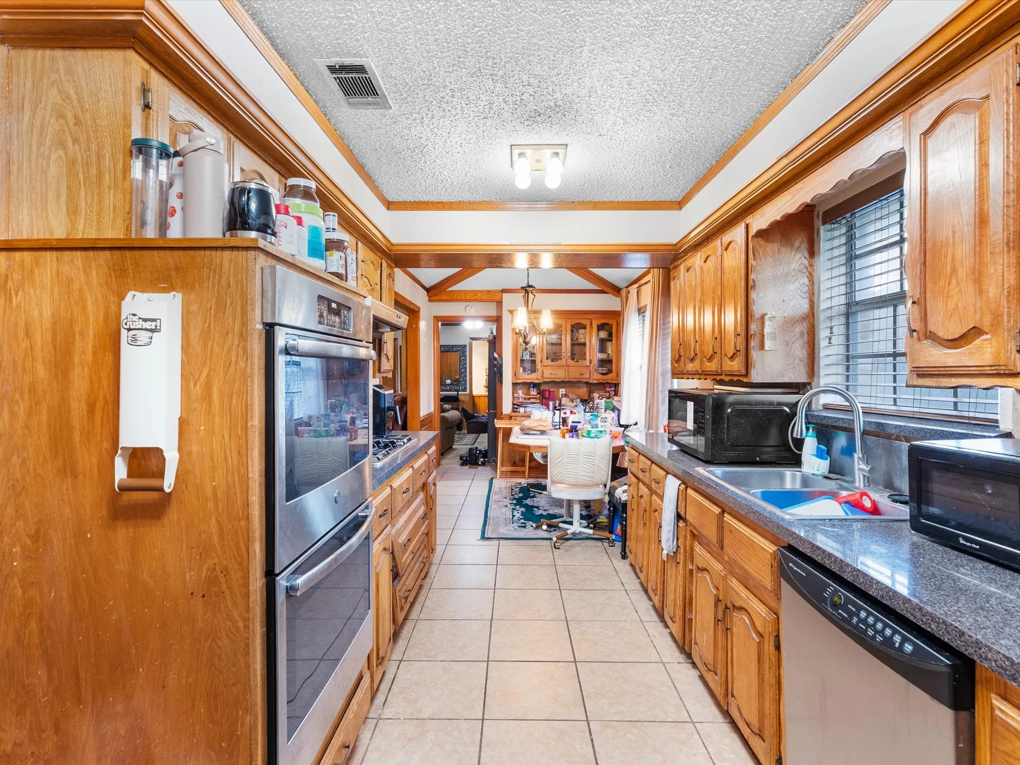 Galley kitchen featuring wood cabinetry, stainless steel double ovens, tile flooring, and a window for natural light