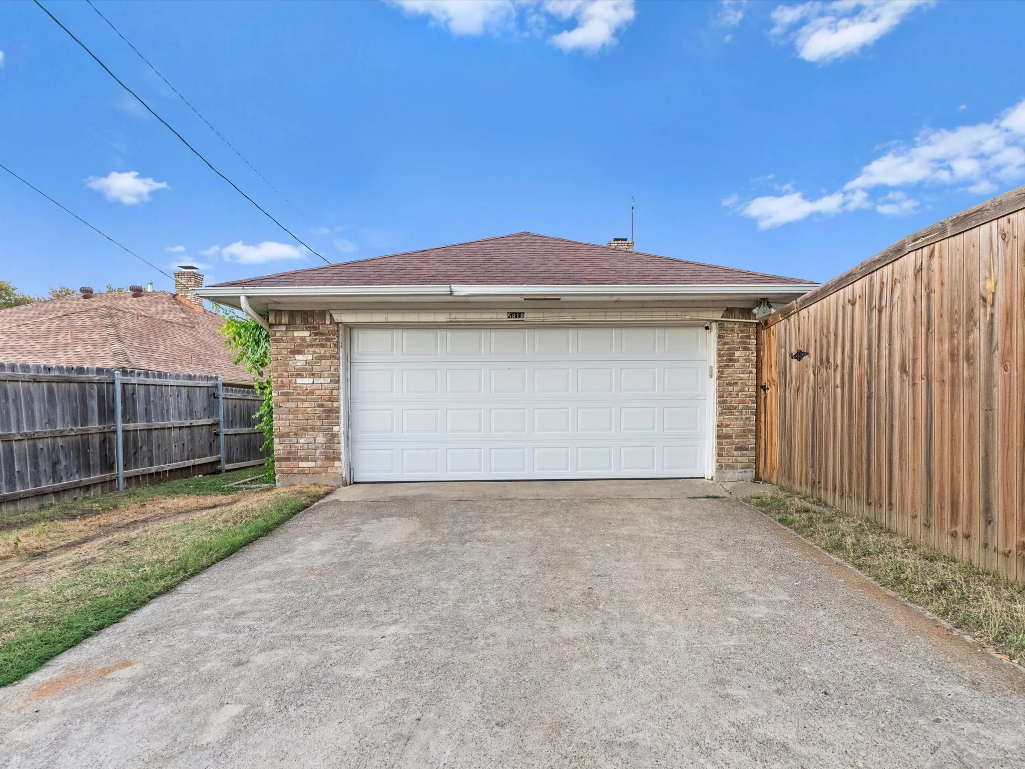 Attached garage with a white panel door, brick facade, and concrete driveway