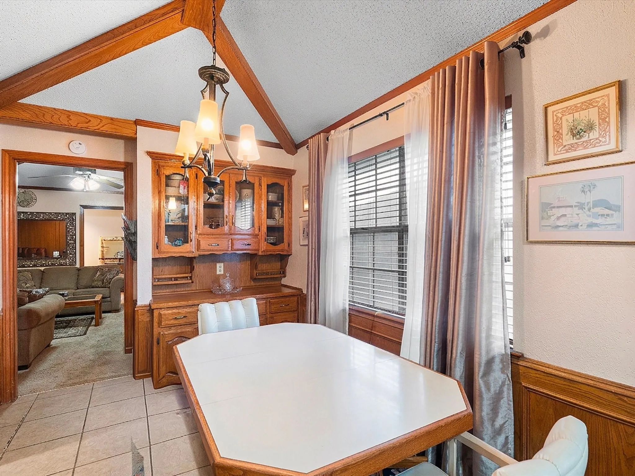 Vaulted ceiling with wood beams, tiled flooring, wood wainscoting, and a built-in wood hutch with glass-front cabinets