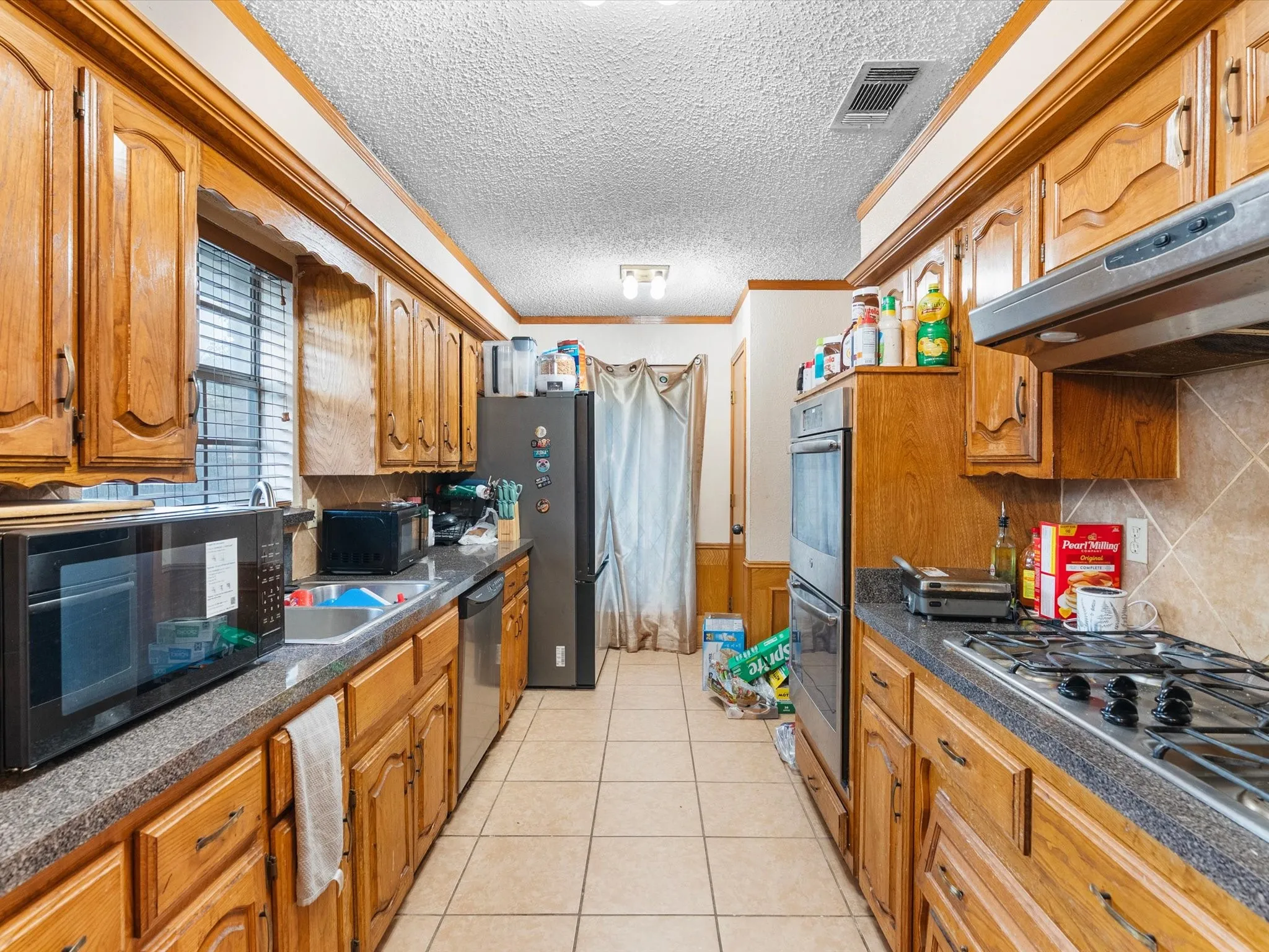 Galley kitchen featuring wood cabinetry, stone-finish countertops, and built-in double ovens
