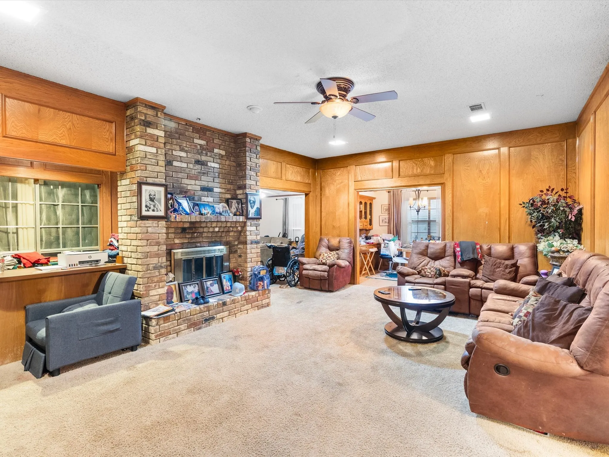 Brick fireplace with hearth, wood-paneled walls, ceiling fan with integrated lighting, wet bar by the fireplace.