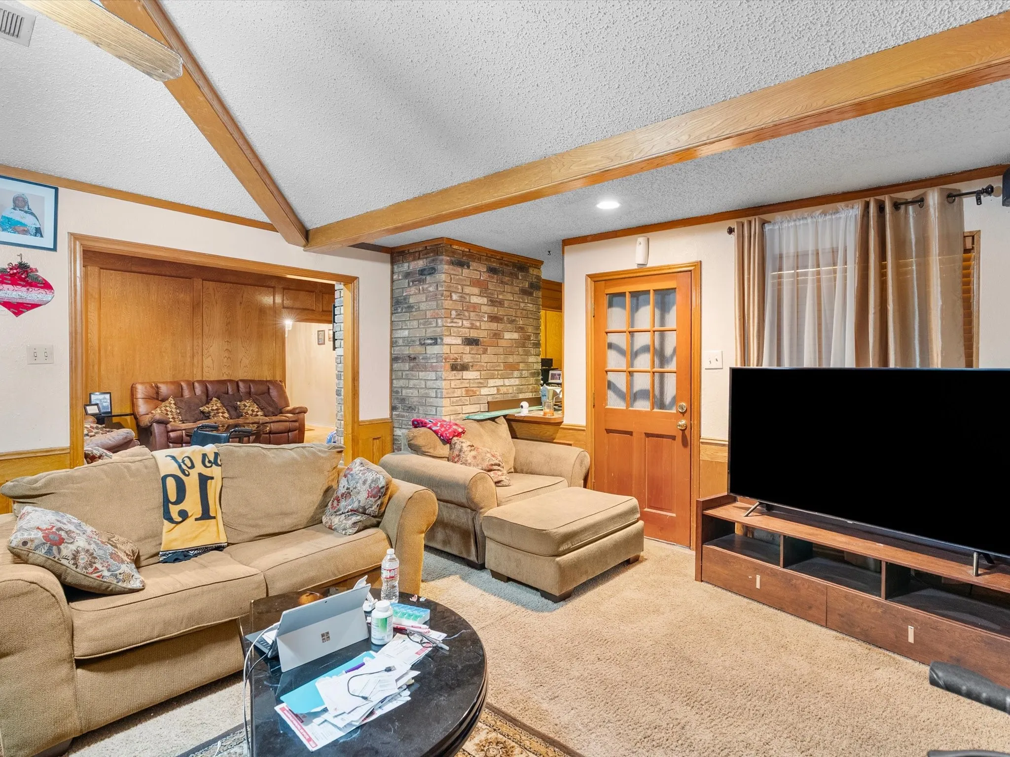 Exposed ceiling beams, brick accent wall, wood-paneled wall, wood-finish interior door with glass inserts, recessed lighting